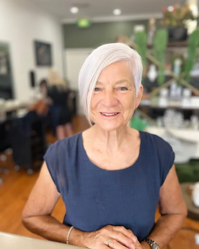 Woman over 60 with a very short platinum-silver asymmetrical bob, longer on one side and swept across the forehead