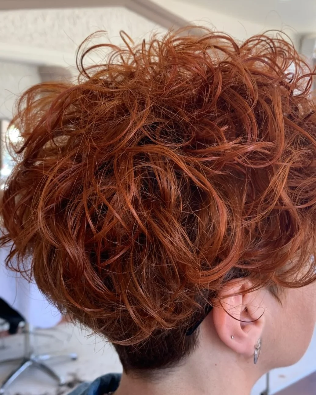 Woman with an edgy curly pixie featuring natural curls on top and shaved sides