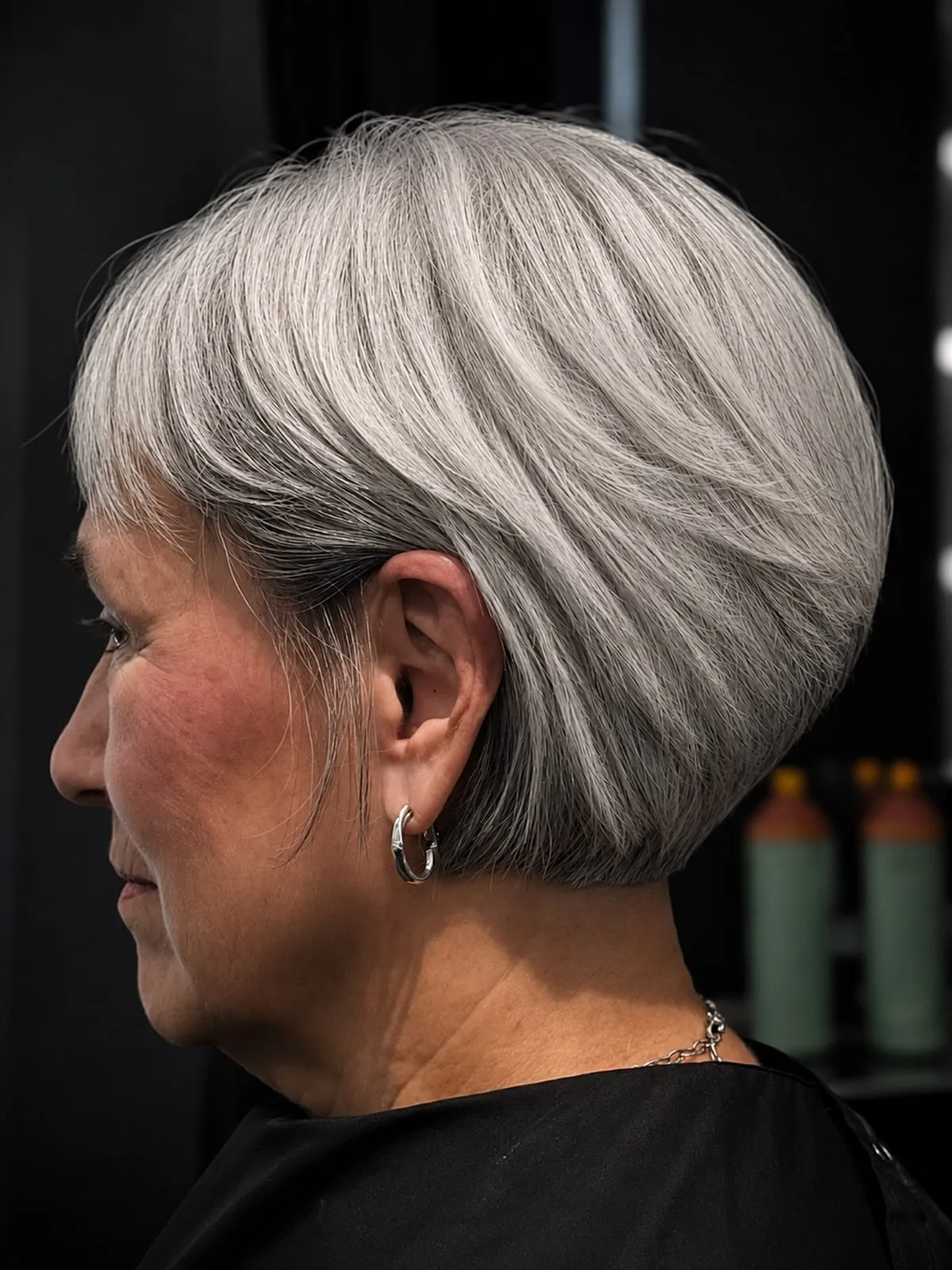 Woman over 50 with a silver-gray layered bob, softly tapered at the nape, seen in side profile.