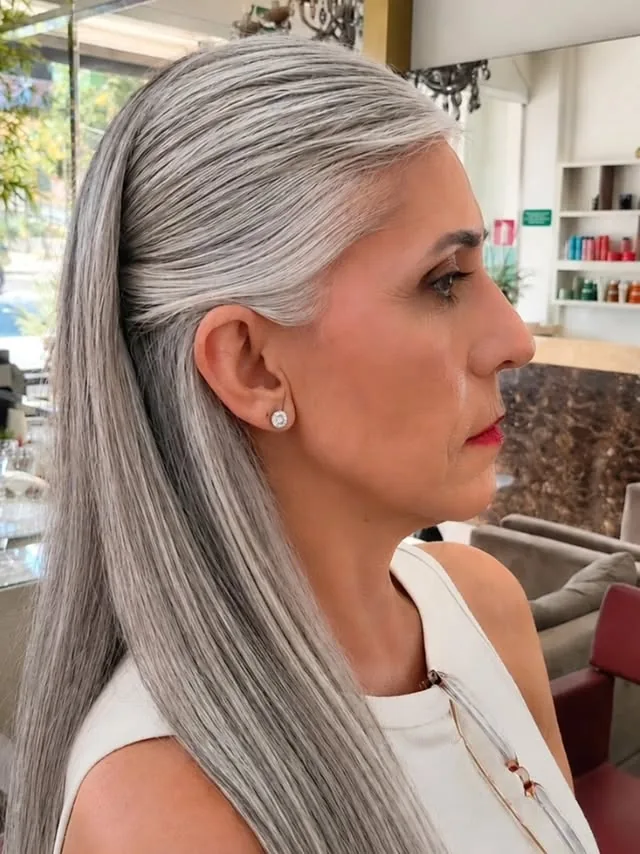 Woman over 50 with long silver-grey hair styled in a sleek low ponytail