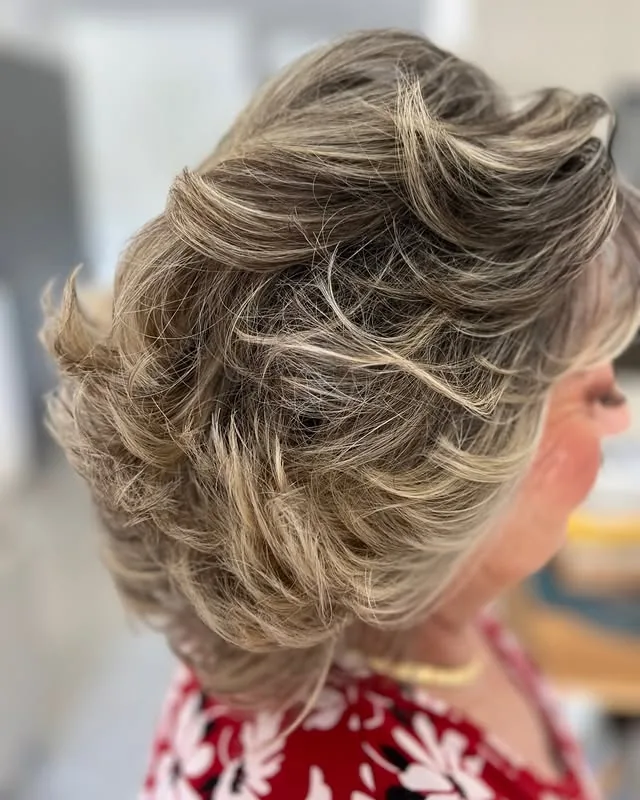 Older woman with a voluminous gray-blonde updo with deliberate lift at the crown