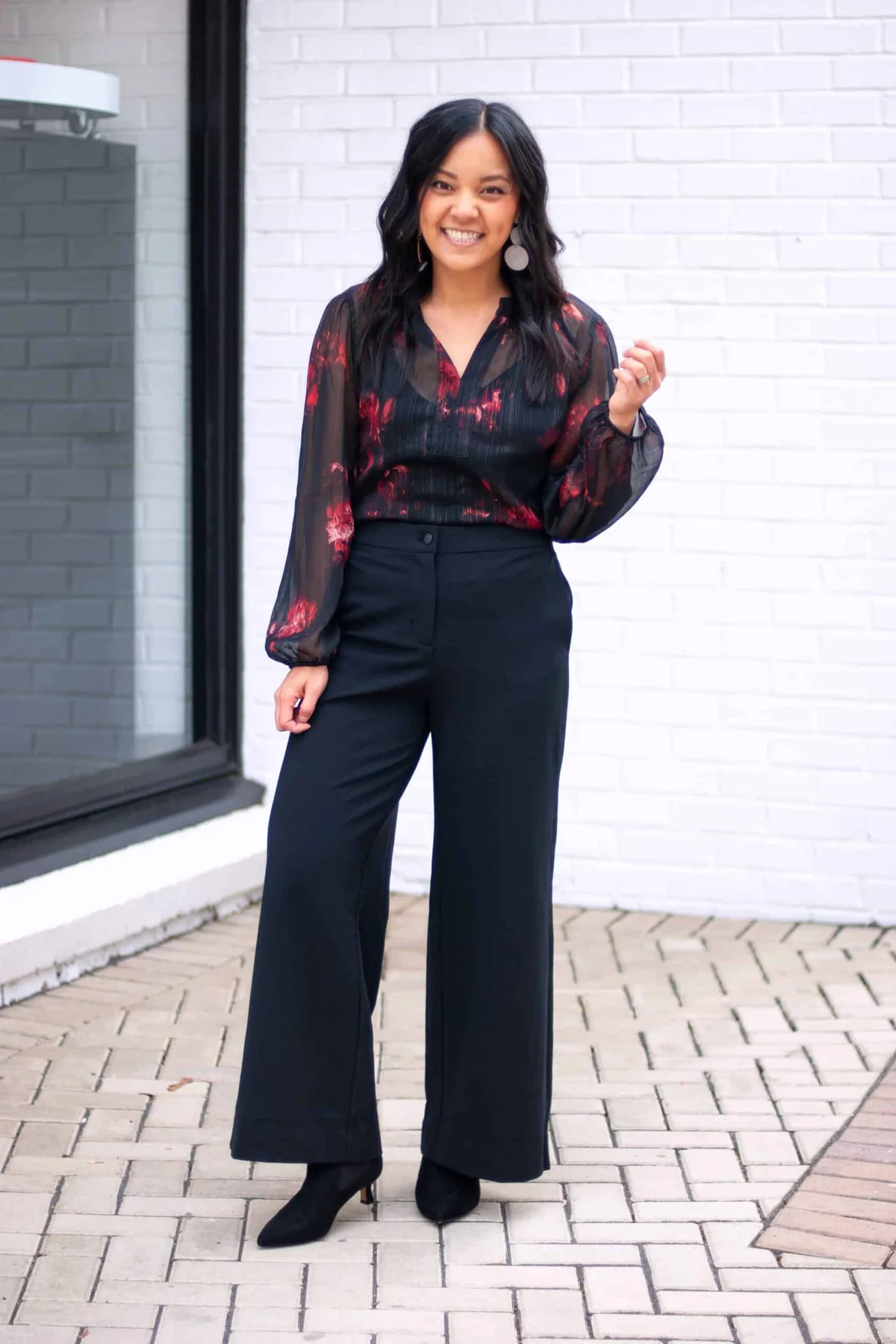A woman wears a red floral V-neck blouse with black wide-leg trousers and pointed boots.