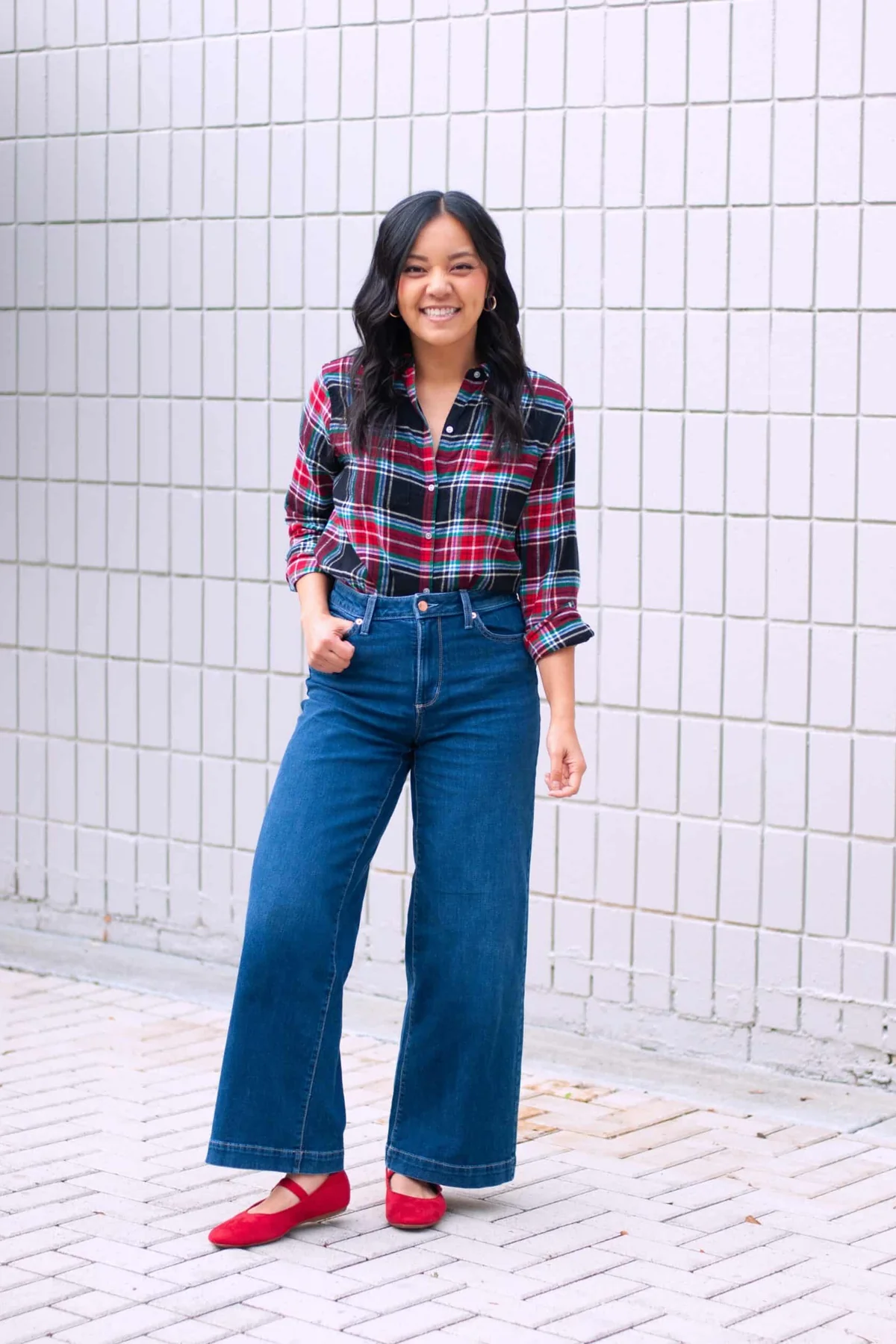 A woman wears a red plaid shirt with wide-leg jeans and red Mary Jane flats.