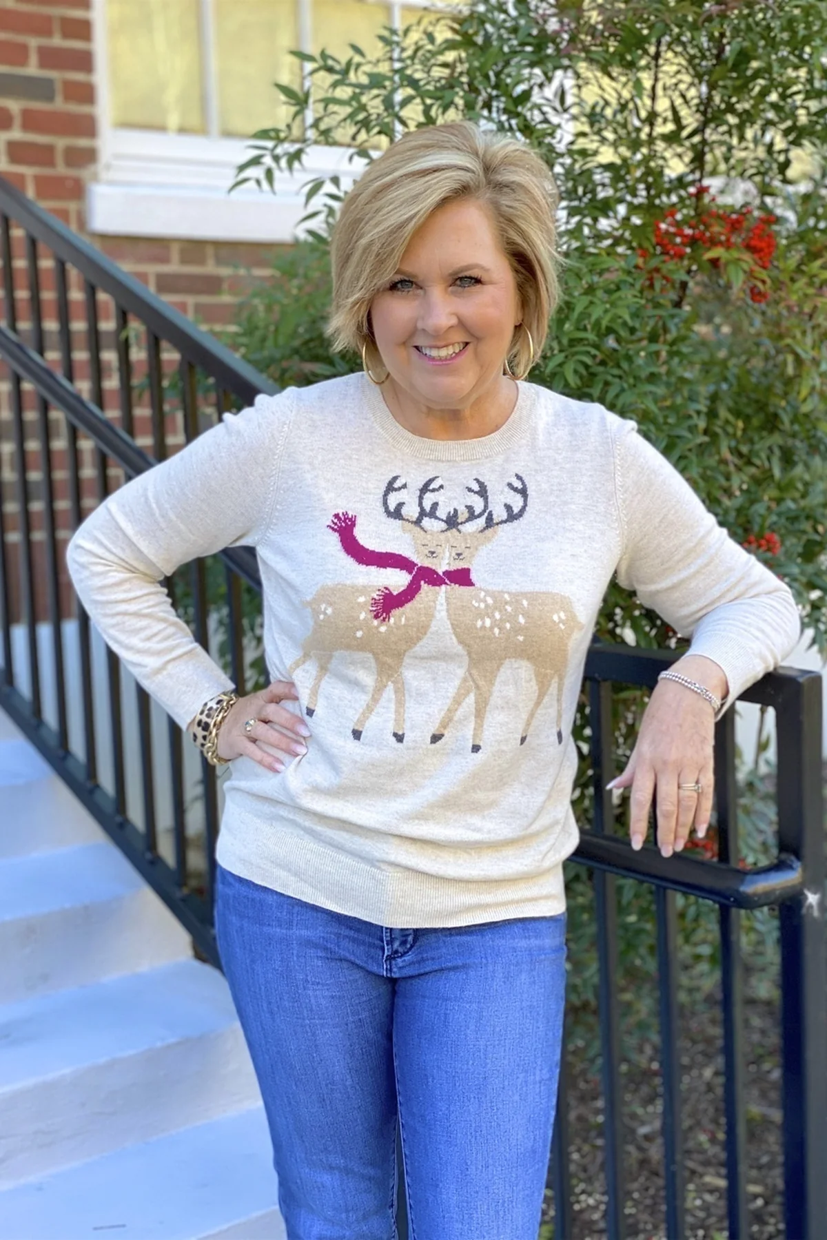 A woman over 50 wears a cream reindeer-motif sweater with blue jeans.
