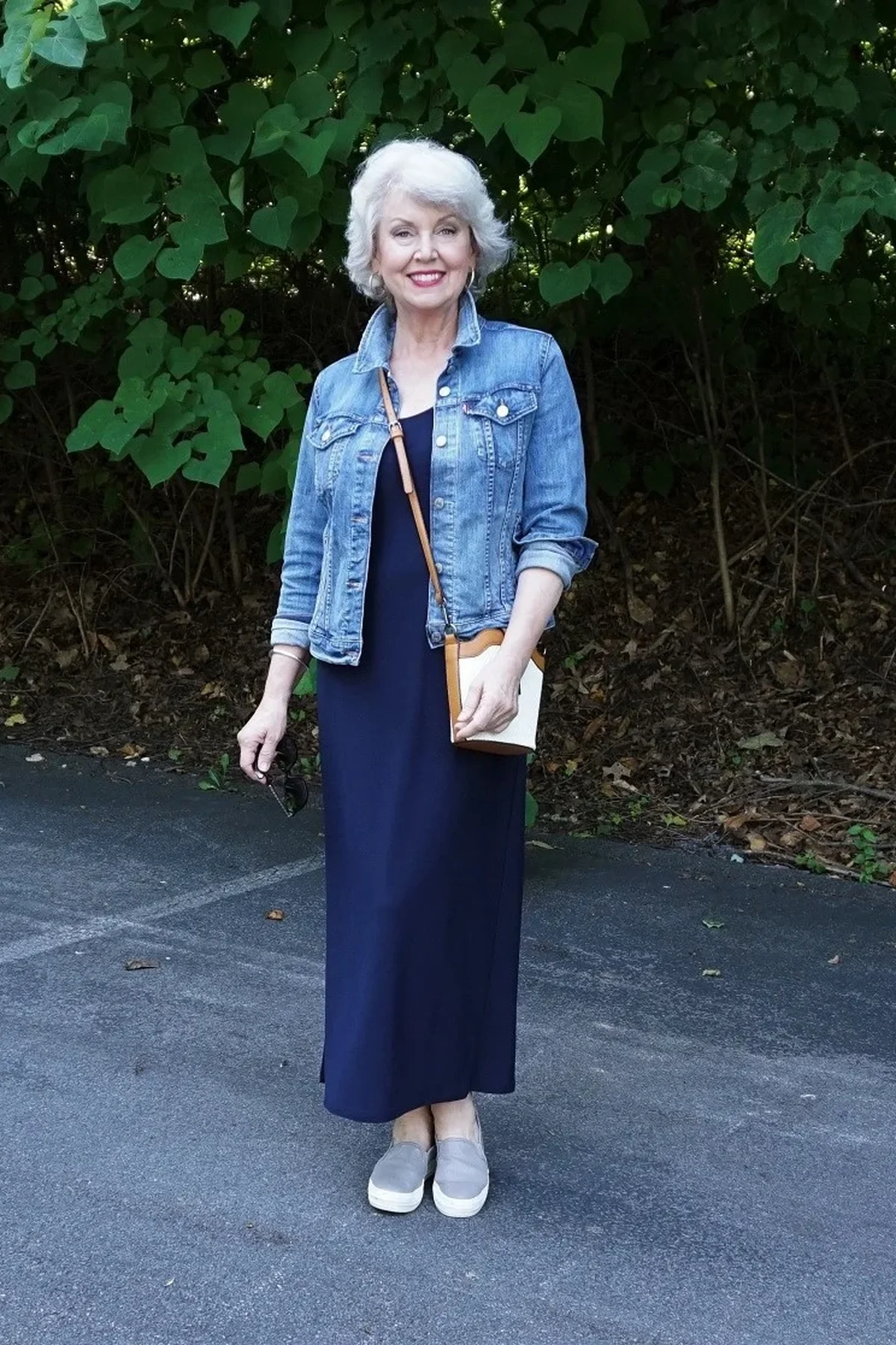 A woman over 50 wears a navy V-neck maxi dress with an open denim jacket outdoors.