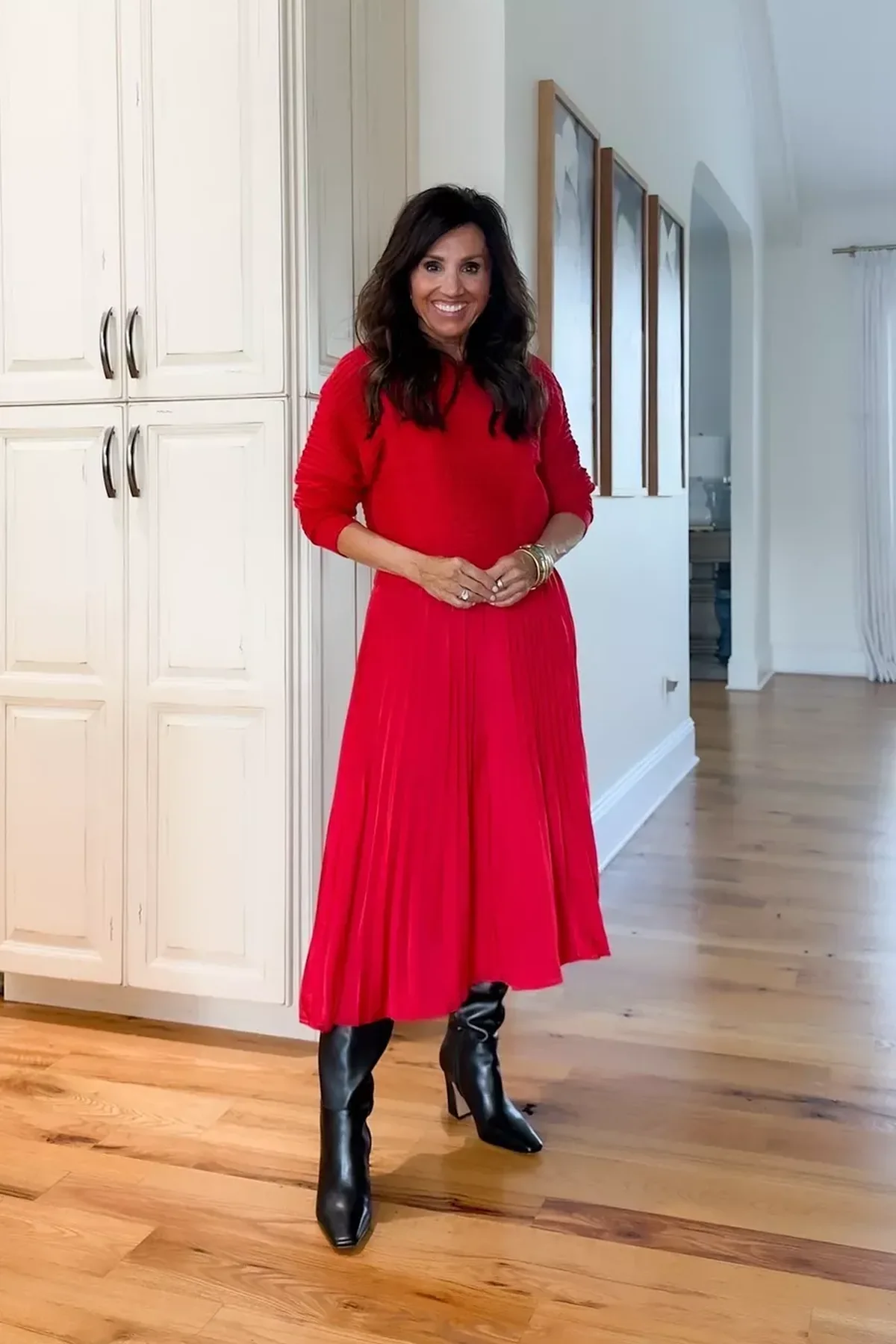 A woman wears a red sweater with a red pleated midi skirt and black knee boots.