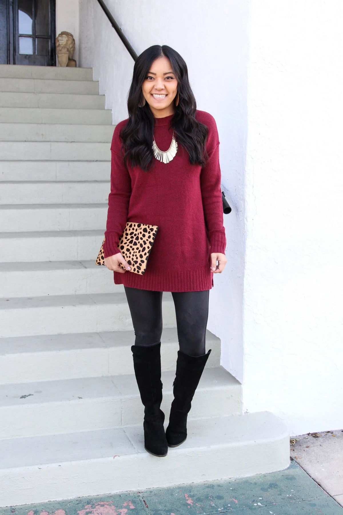 Woman in burgundy knit tunic and black leggings with tall boots on outdoor stairs