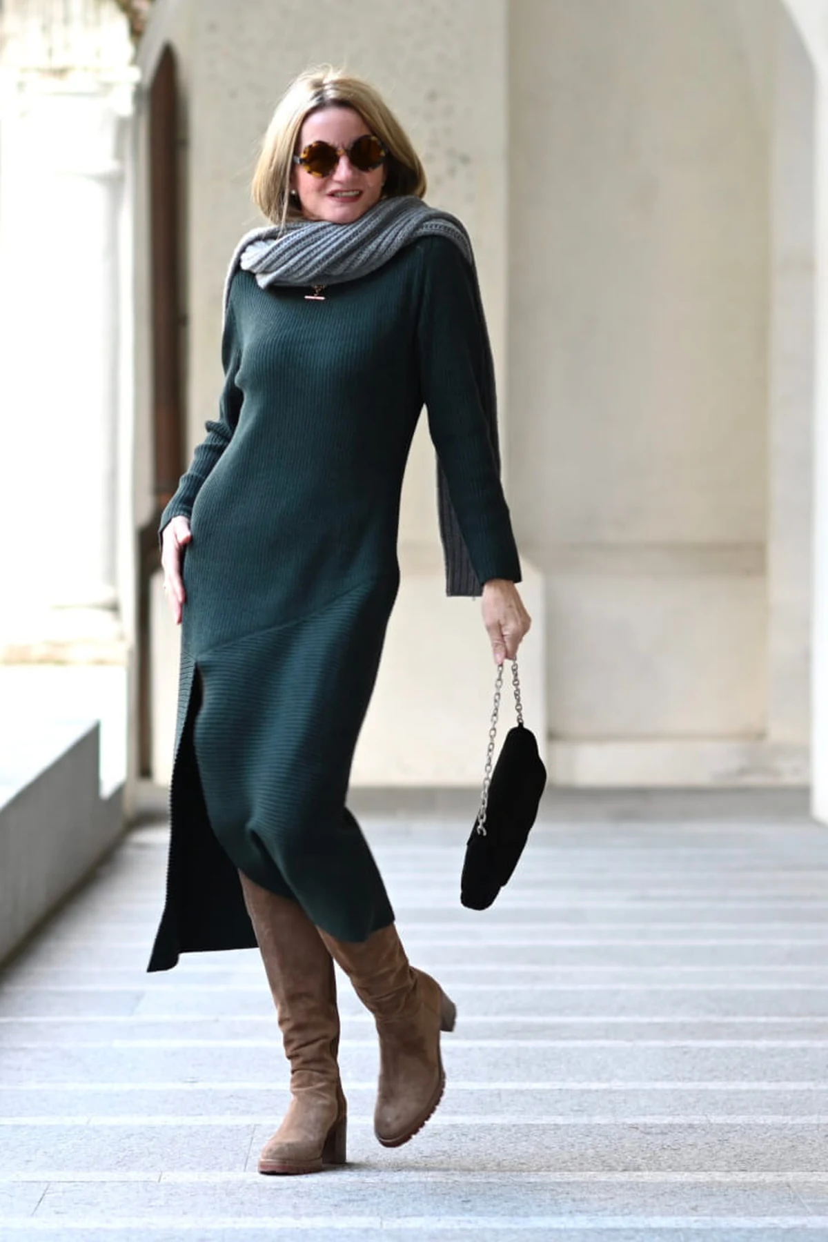 Woman in forest green ribbed midi dress and gray scarf walking through a colonnade