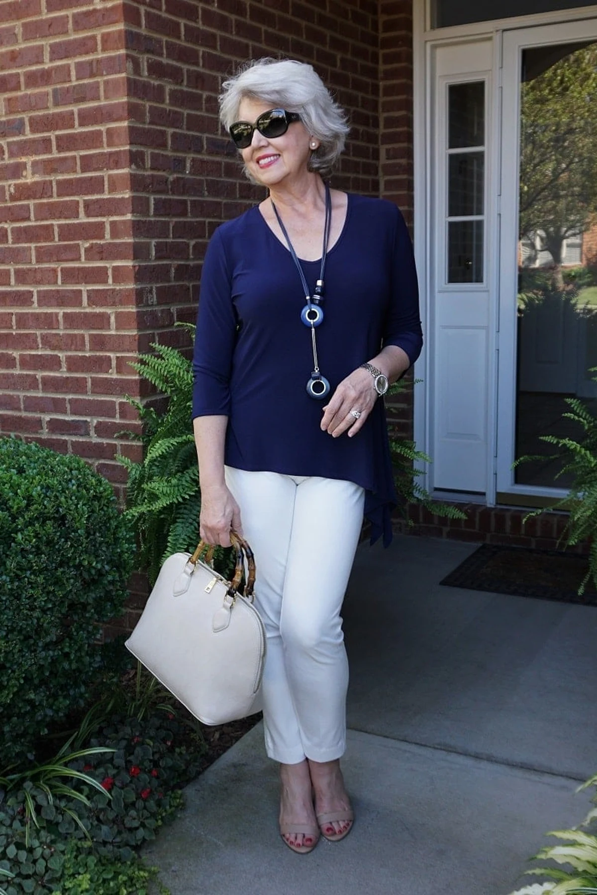 Woman in navy tunic and white cropped trousers on a brick porch