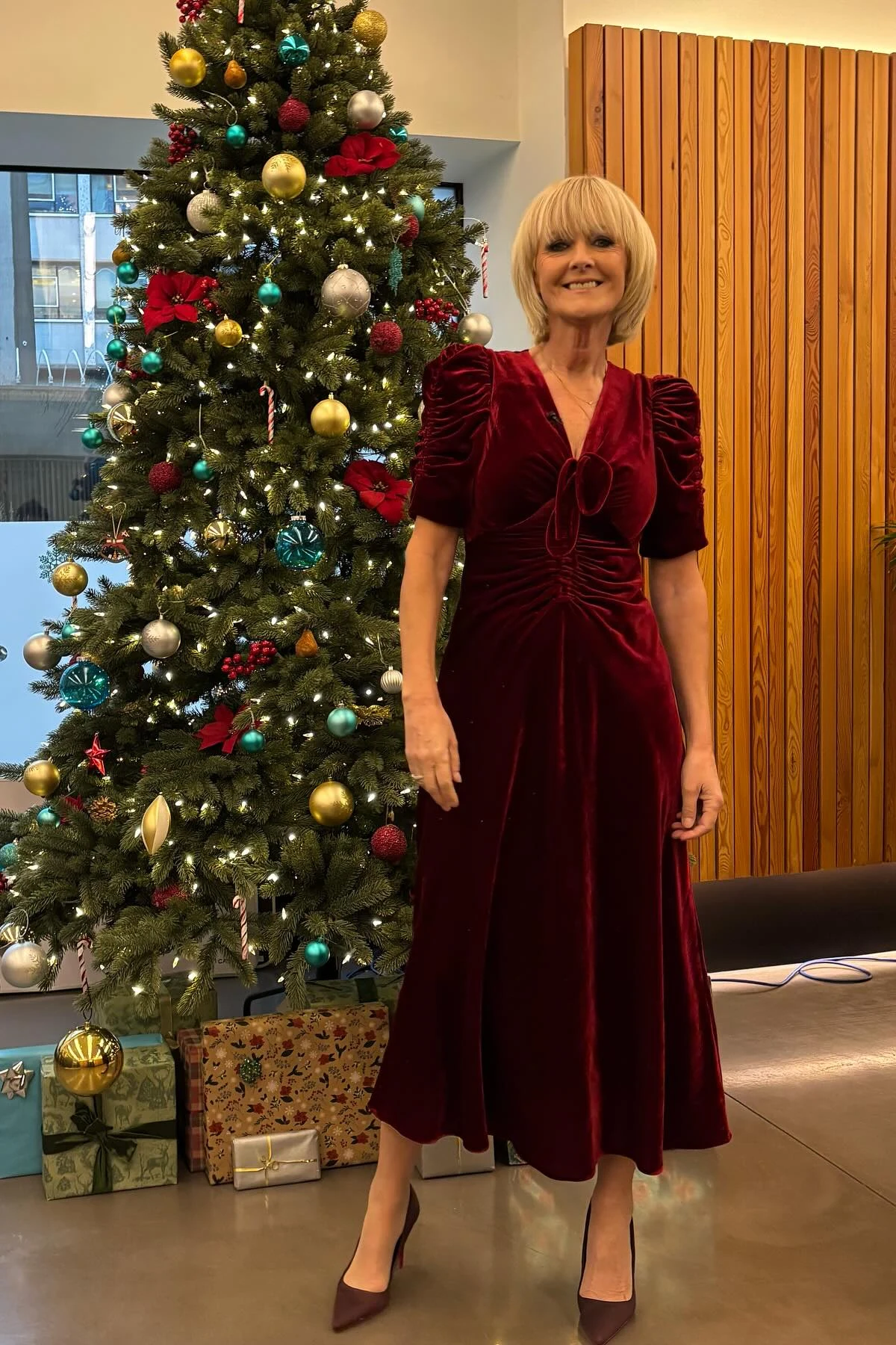 Woman in plum velvet midi dress beside a Christmas tree with gifts