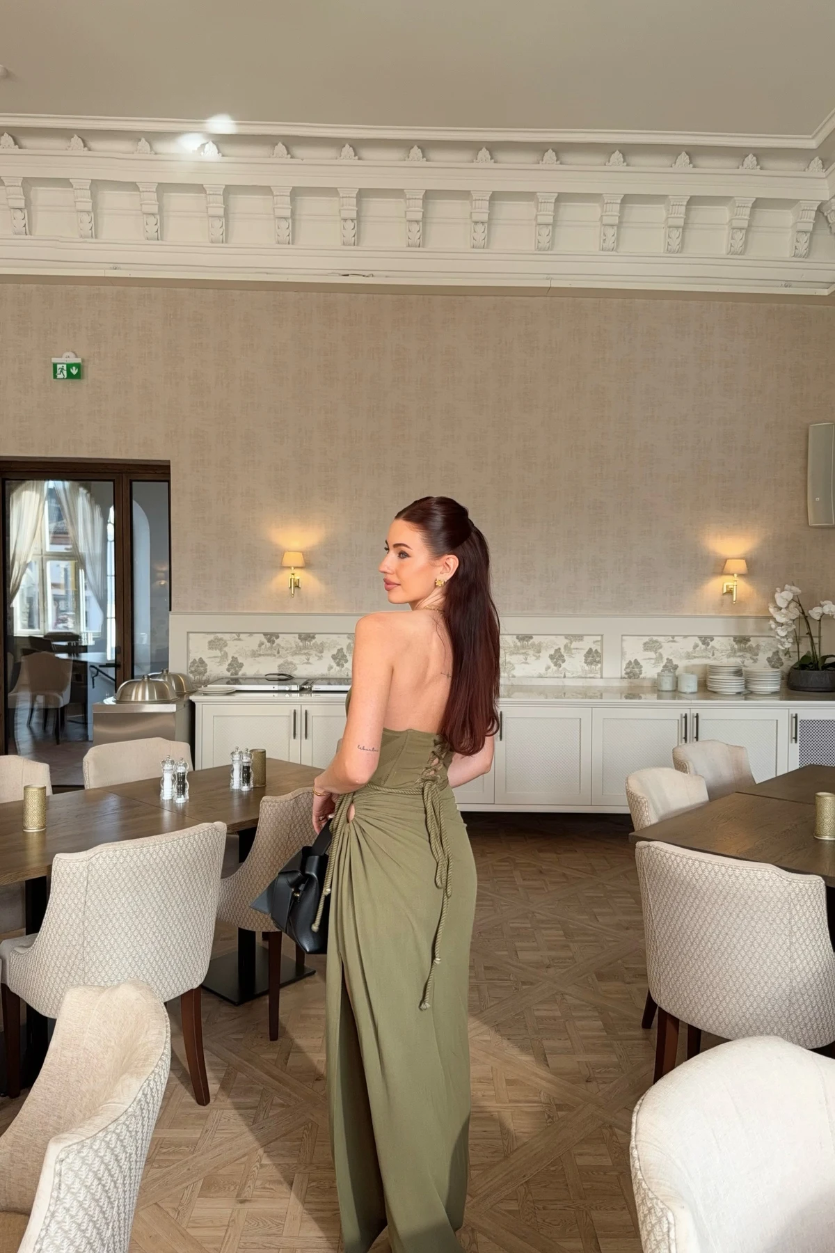 Back view of woman in olive lace-up maxi dress in an elegant restaurant