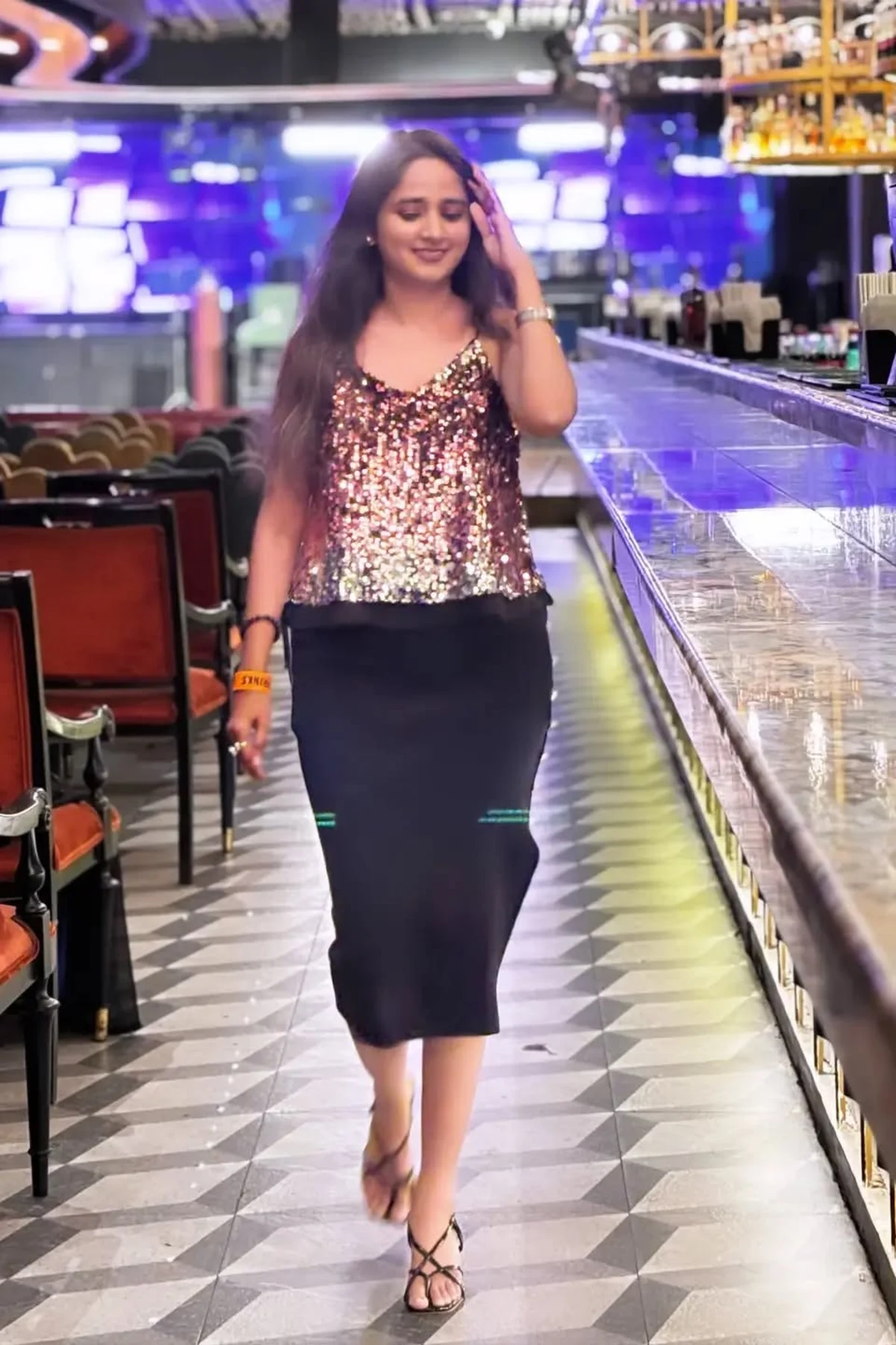 Woman in gold sequin camisole and black midi skirt in a lounge at night