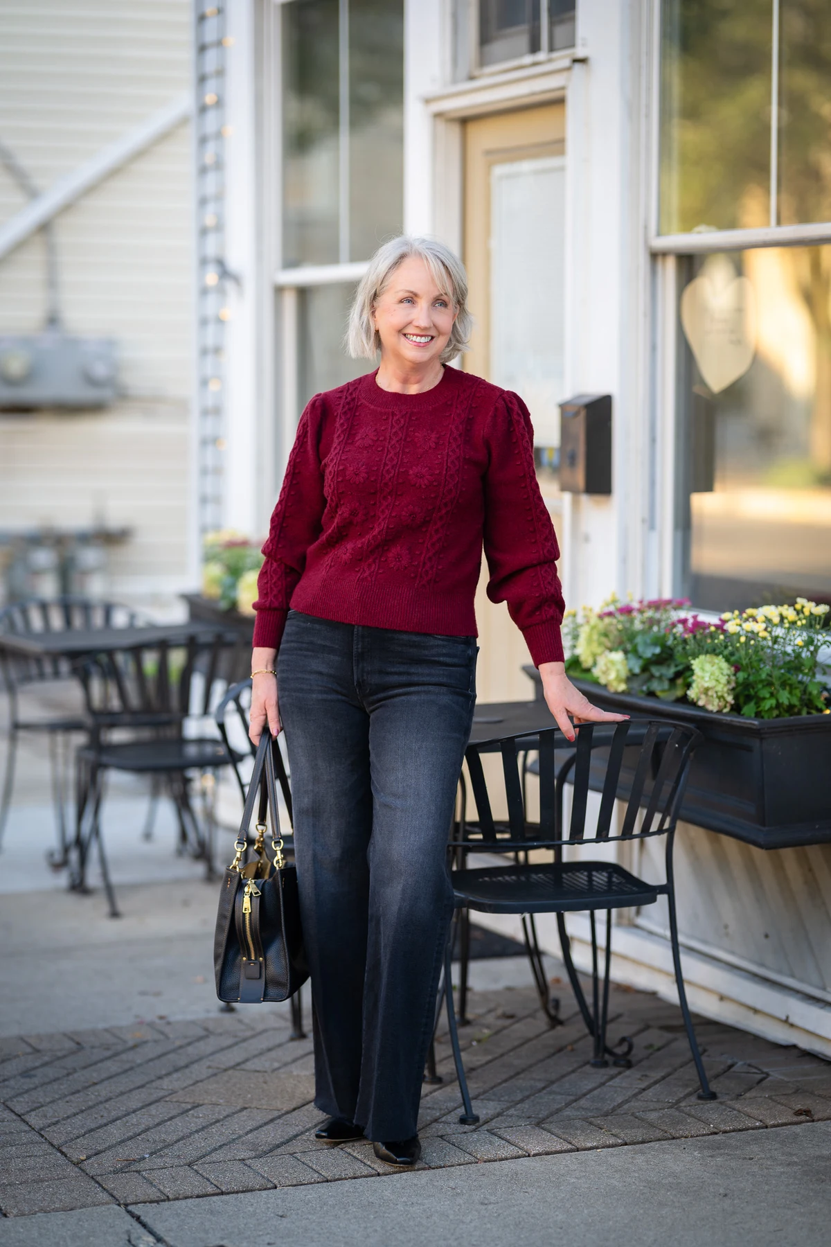 Woman in wine cable-knit sweater and dark jeans at an outdoor cafe
