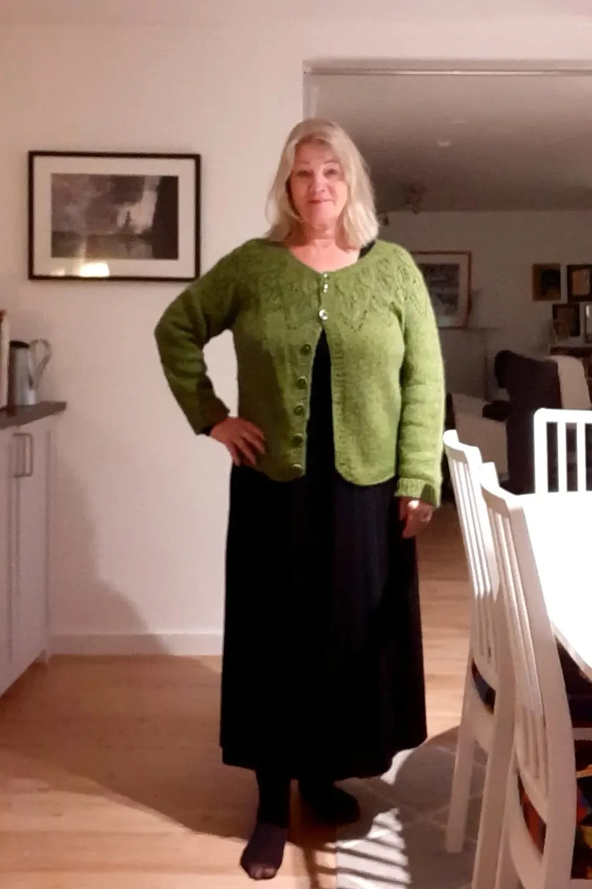 Woman in green knit cardigan and long black dress in a home dining area