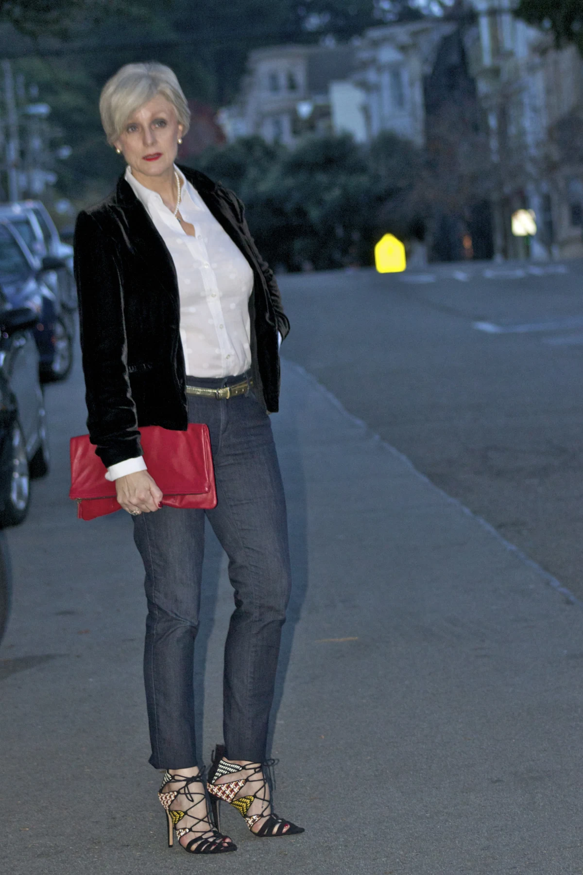 Woman over 50 in a black velvet blazer over a white polka-dot shirt and dark jeans on a San Francisco street at Christmas