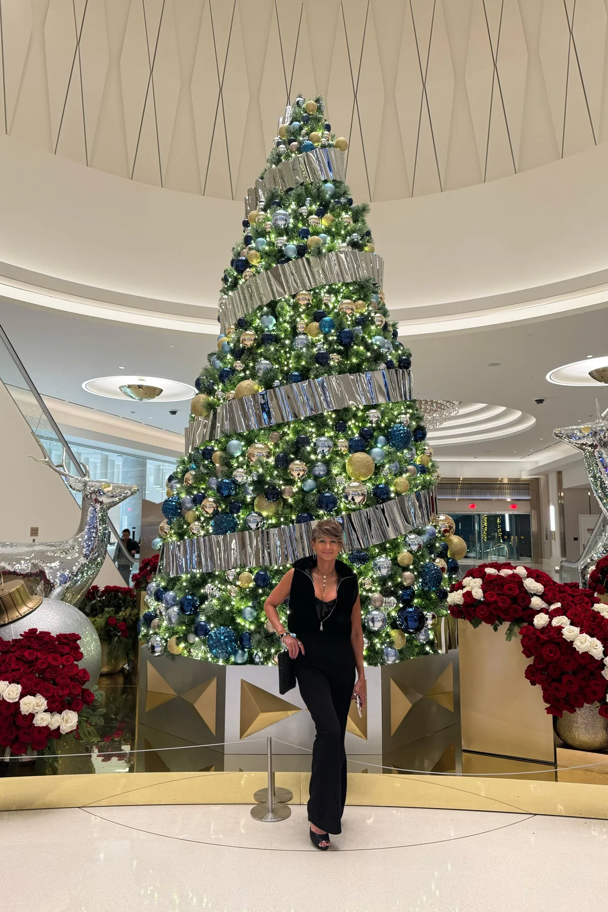 Woman in a black surplice jumpsuit with a deep V-neckline in front of a grand Christmas tree in a hotel lobby