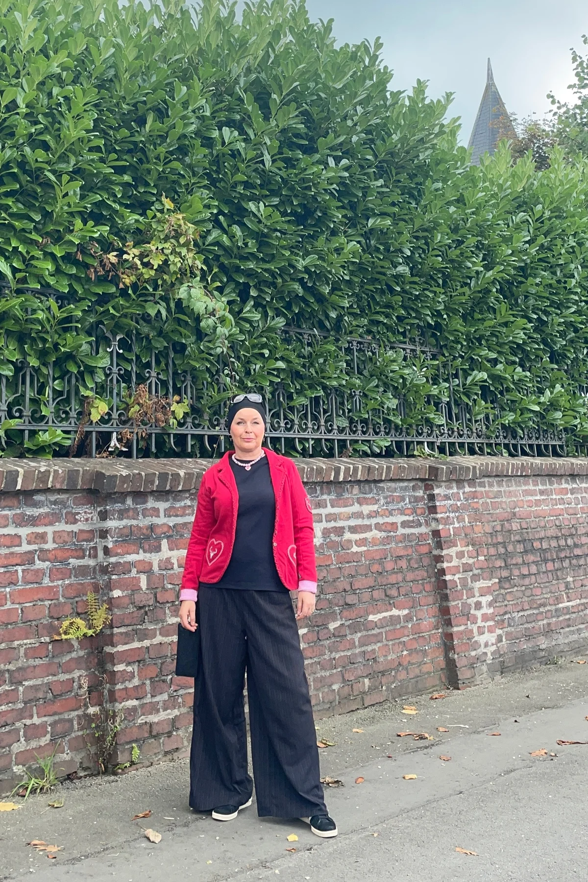 Woman in red knit cardigan and black jeans with black hijab beside a Christmas tree