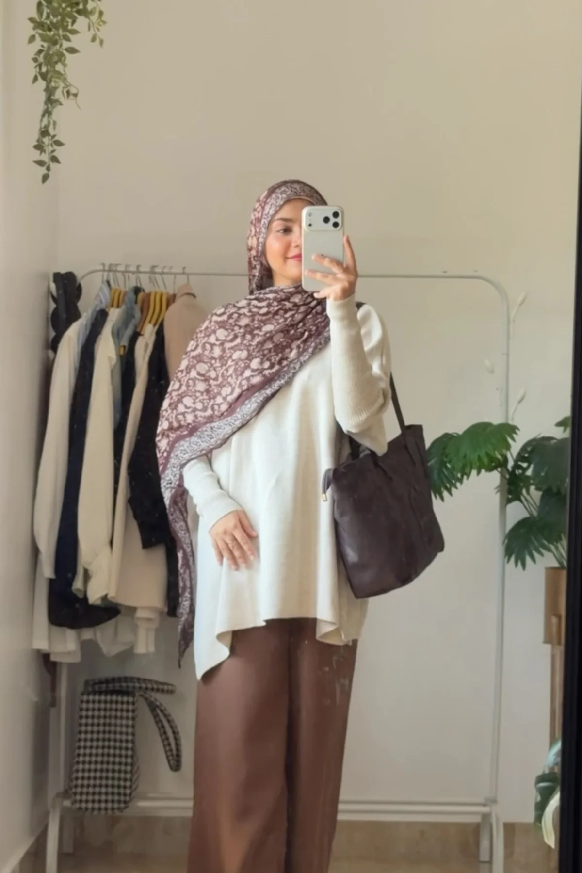 Hijabi woman in cream sweater and camel wide-leg trousers walking past a festive bakery
