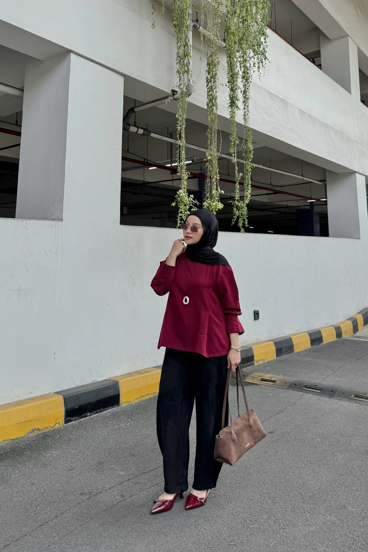 Woman in burgundy tunic blouse and black wide-leg trousers with plum hijab at Christmas
