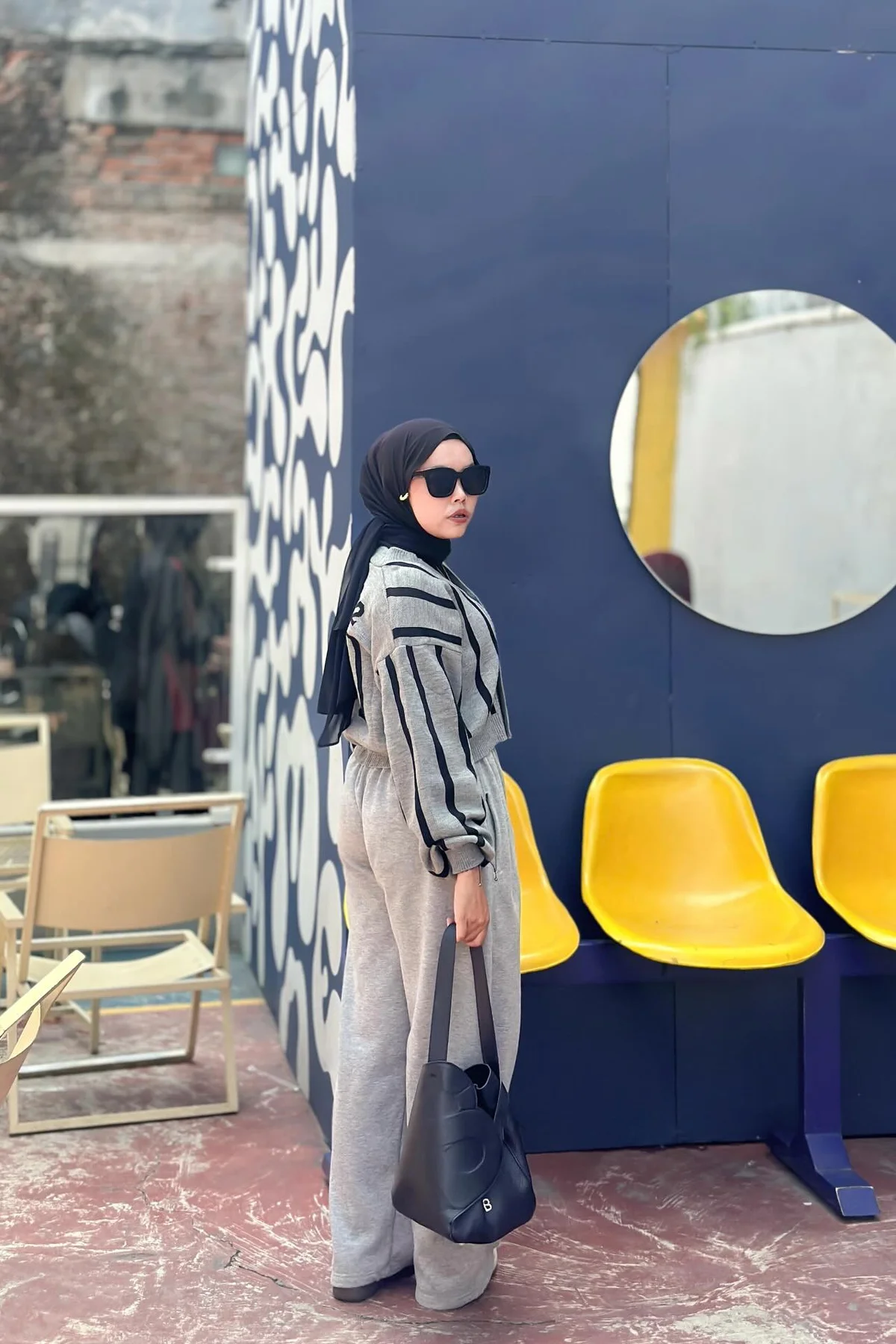Woman in grey zip cardigan, olive joggers and black hijab carrying a gift at a Christmas market