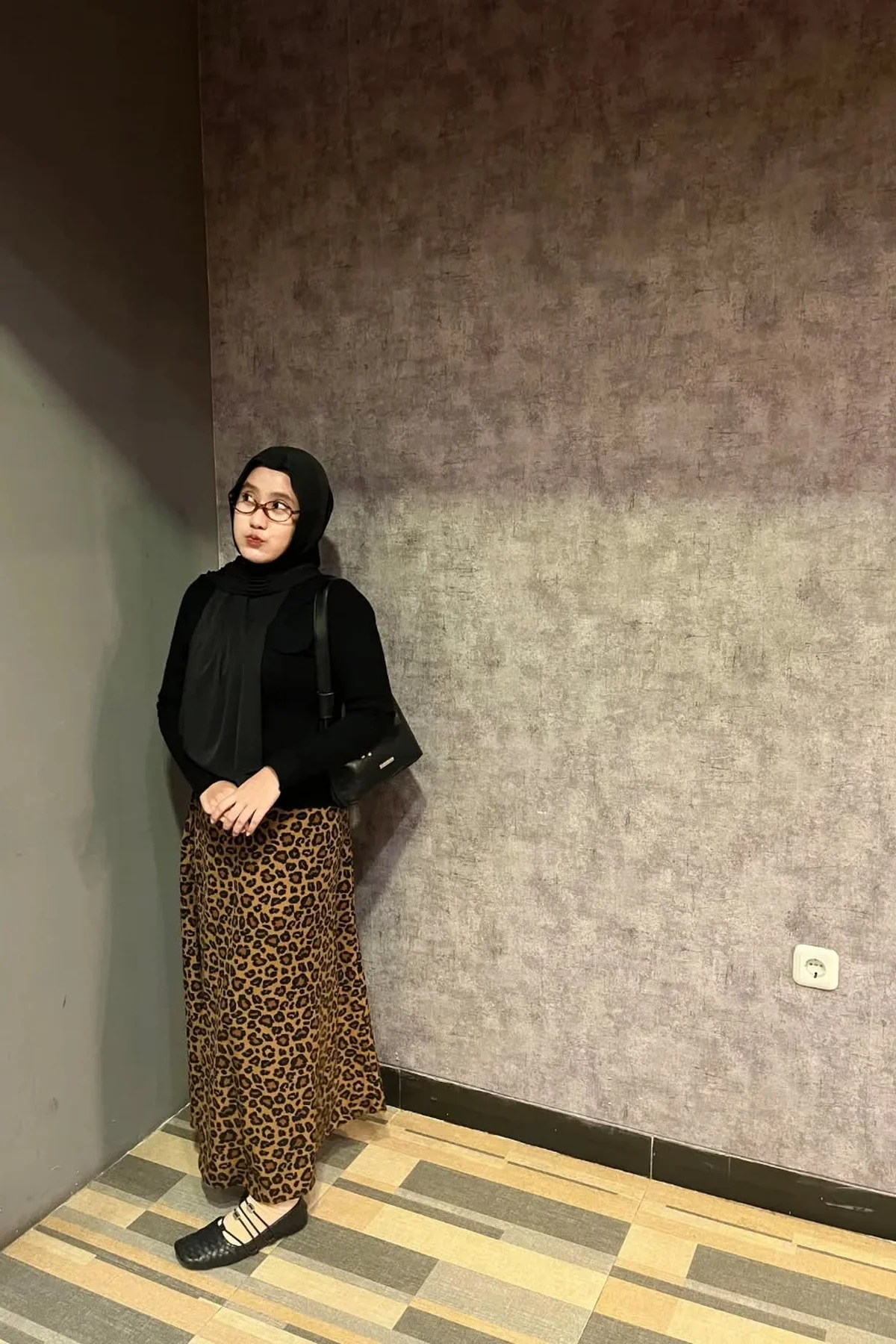 Hijabi woman in leopard pleated maxi skirt and black turtleneck at a candlelit Christmas shopfront