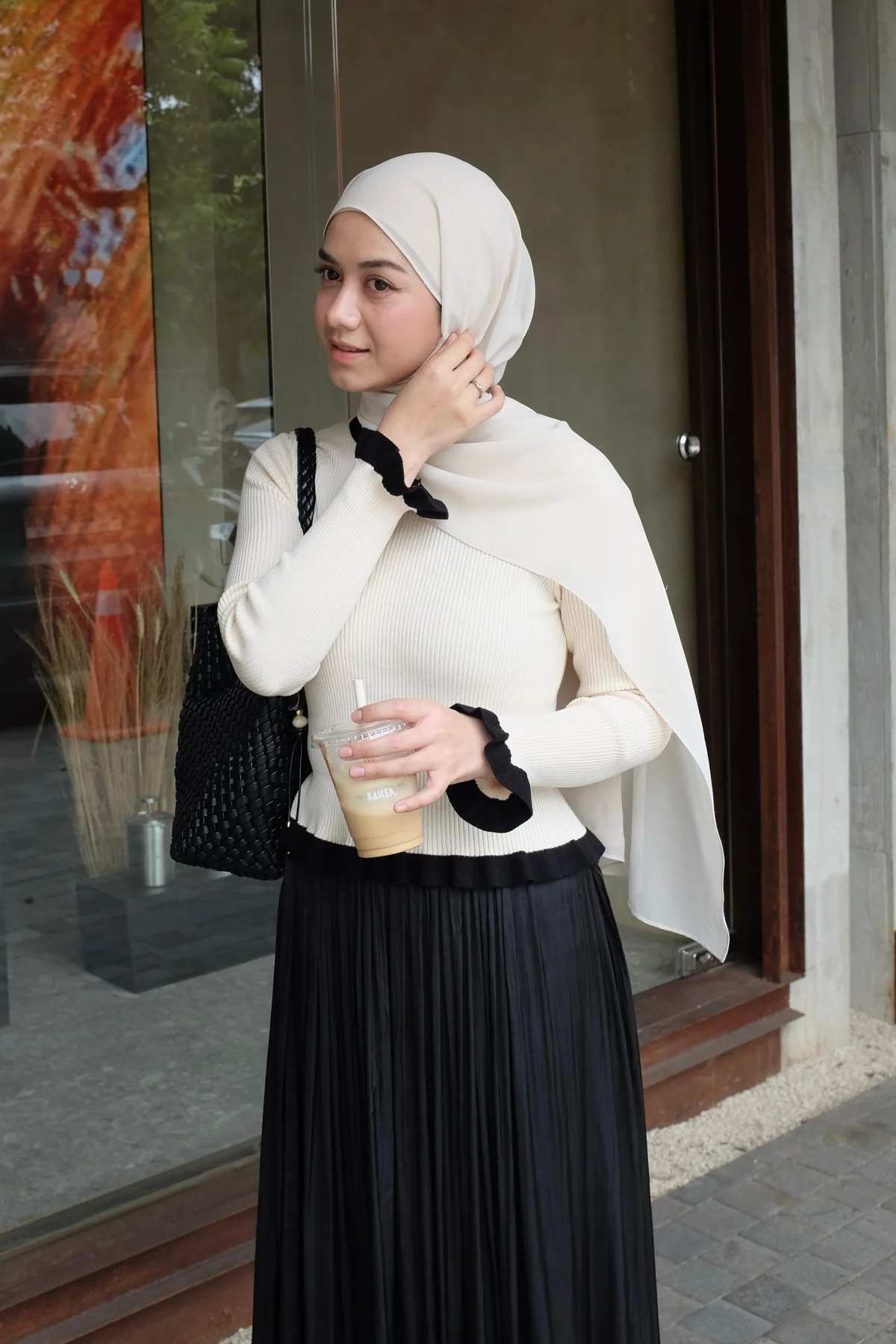 Woman in cream sweater and black faux-leather maxi skirt with hijab beside a Christmas tree