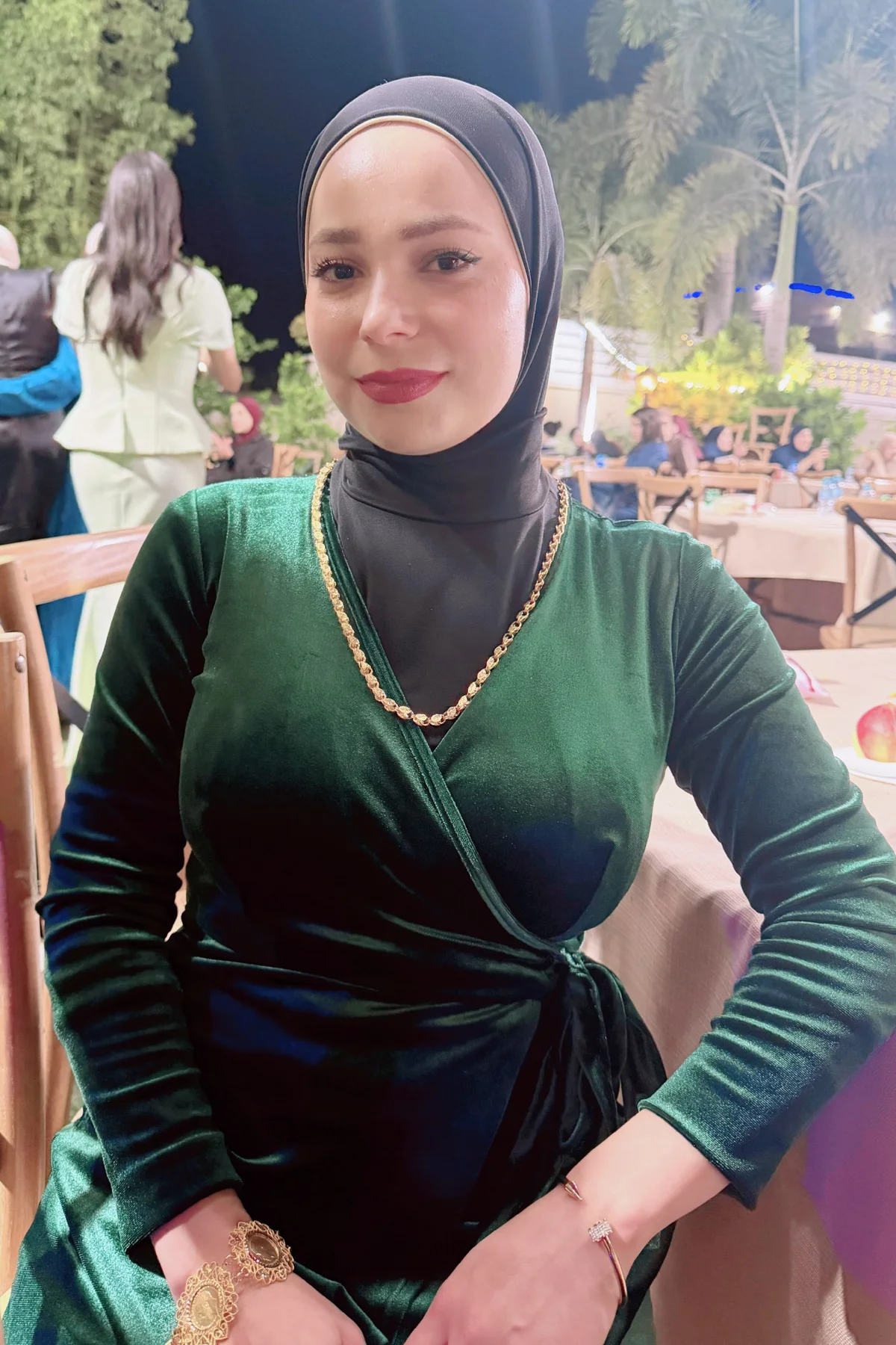 Hijabi woman in emerald velvet maxi dress and black satin hijab at a Christmas party