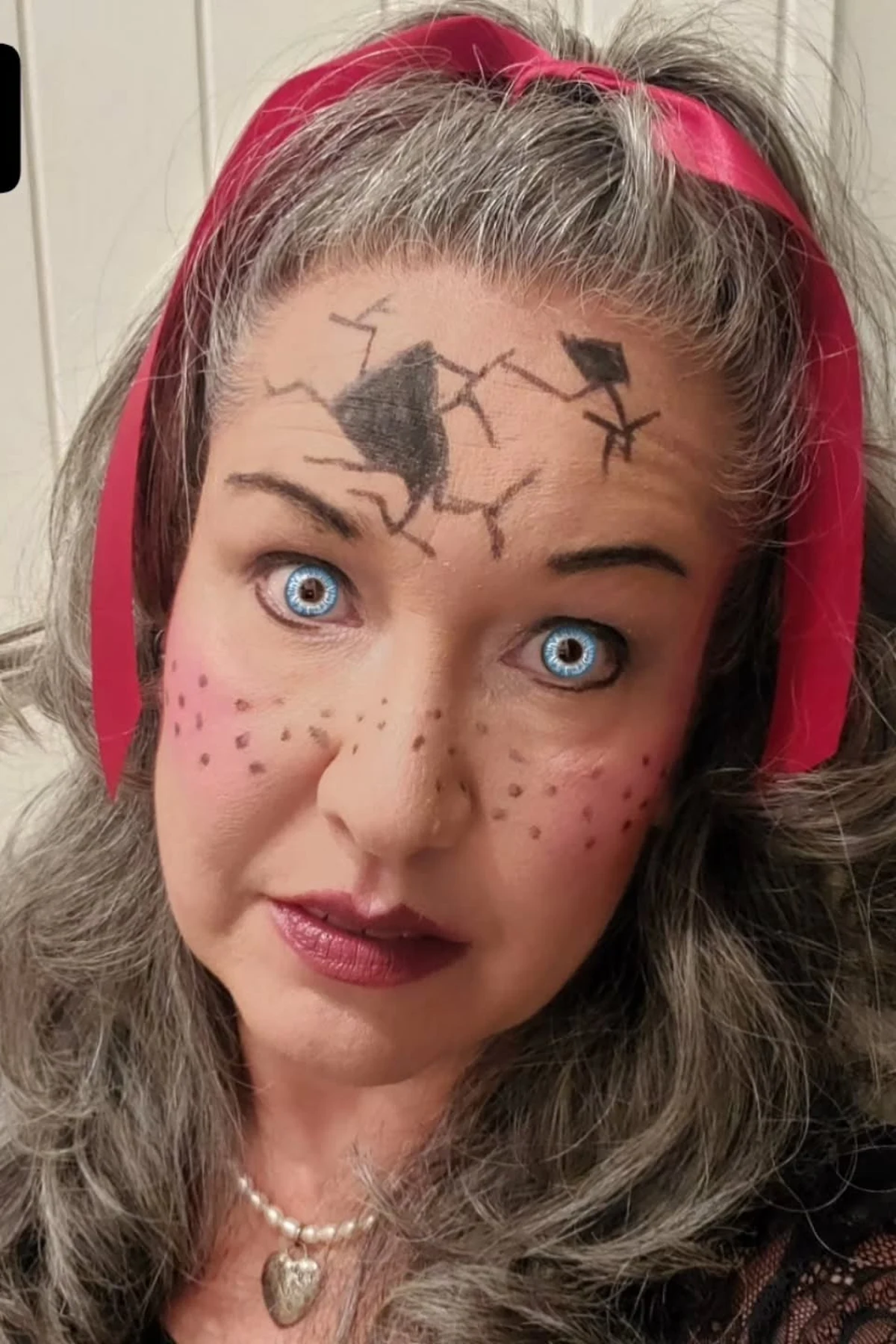 Woman over 50 in a floral dress with cracked porcelain doll face paint, a DIY creepy doll Halloween costume