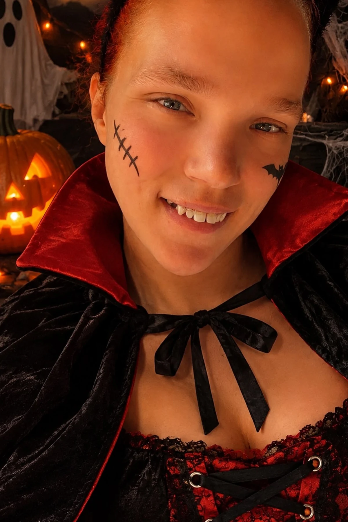Woman over 50 in black with a DIY tablecloth cape and vampire fangs, a DIY vampire Halloween costume