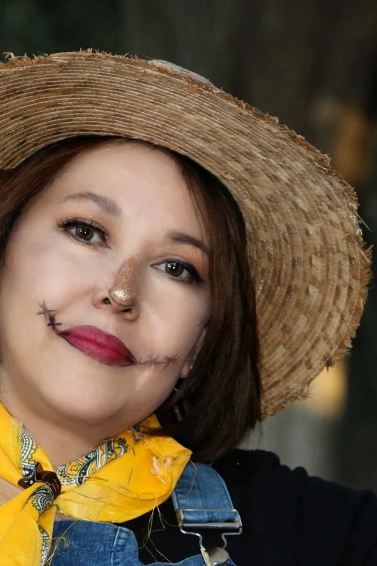 Woman over 50 in overalls holding dead weeds, a DIY creepy gardener Halloween costume