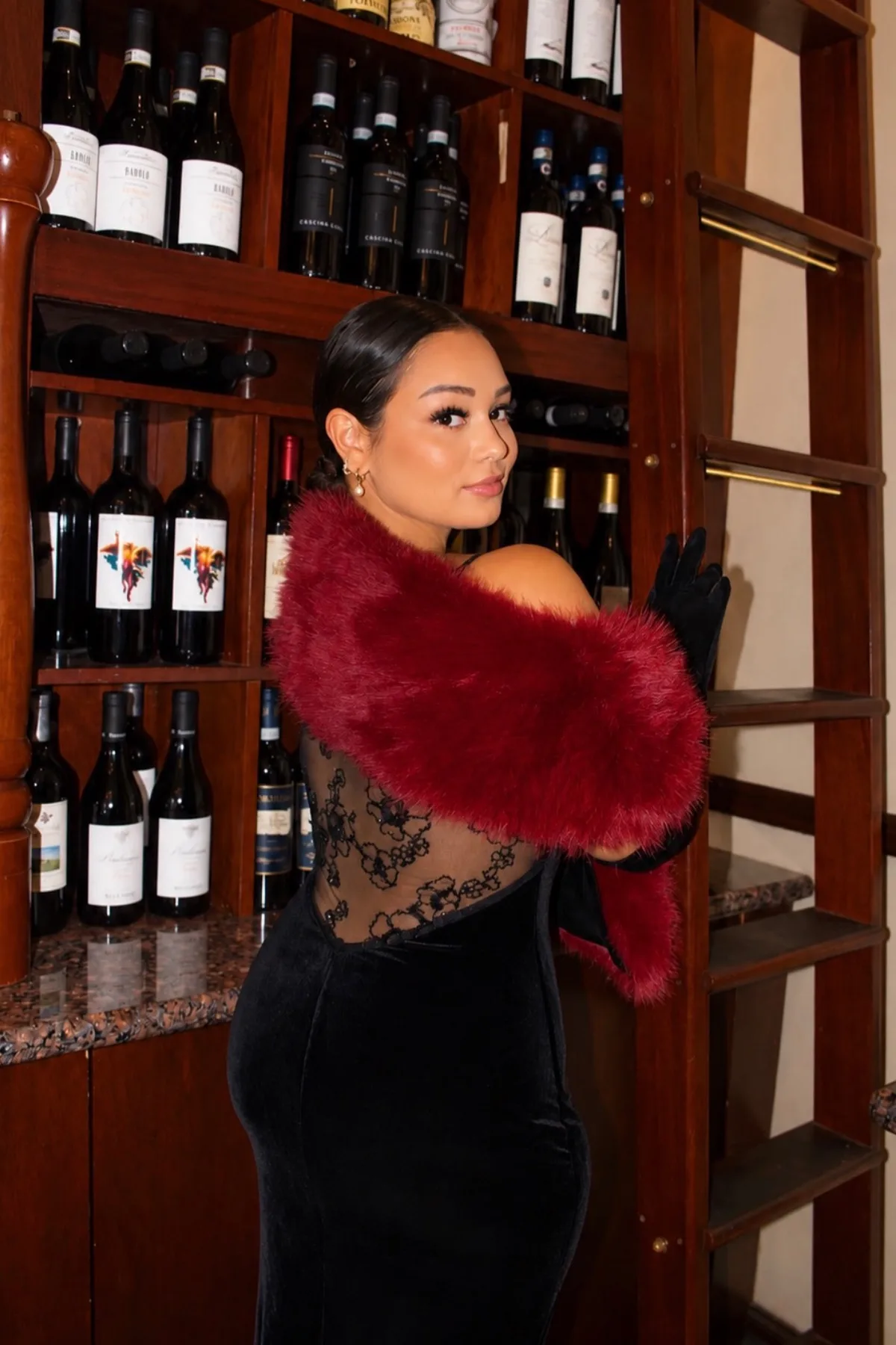 Woman over 50 in a black knit dress and wine faux fur stole, a dark countess gothic Halloween costume.