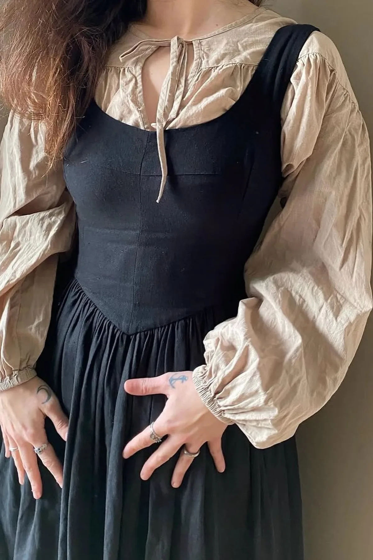 Woman over 50 in a black pinafore over a cream lace blouse, a dark Alice gothic Halloween costume.