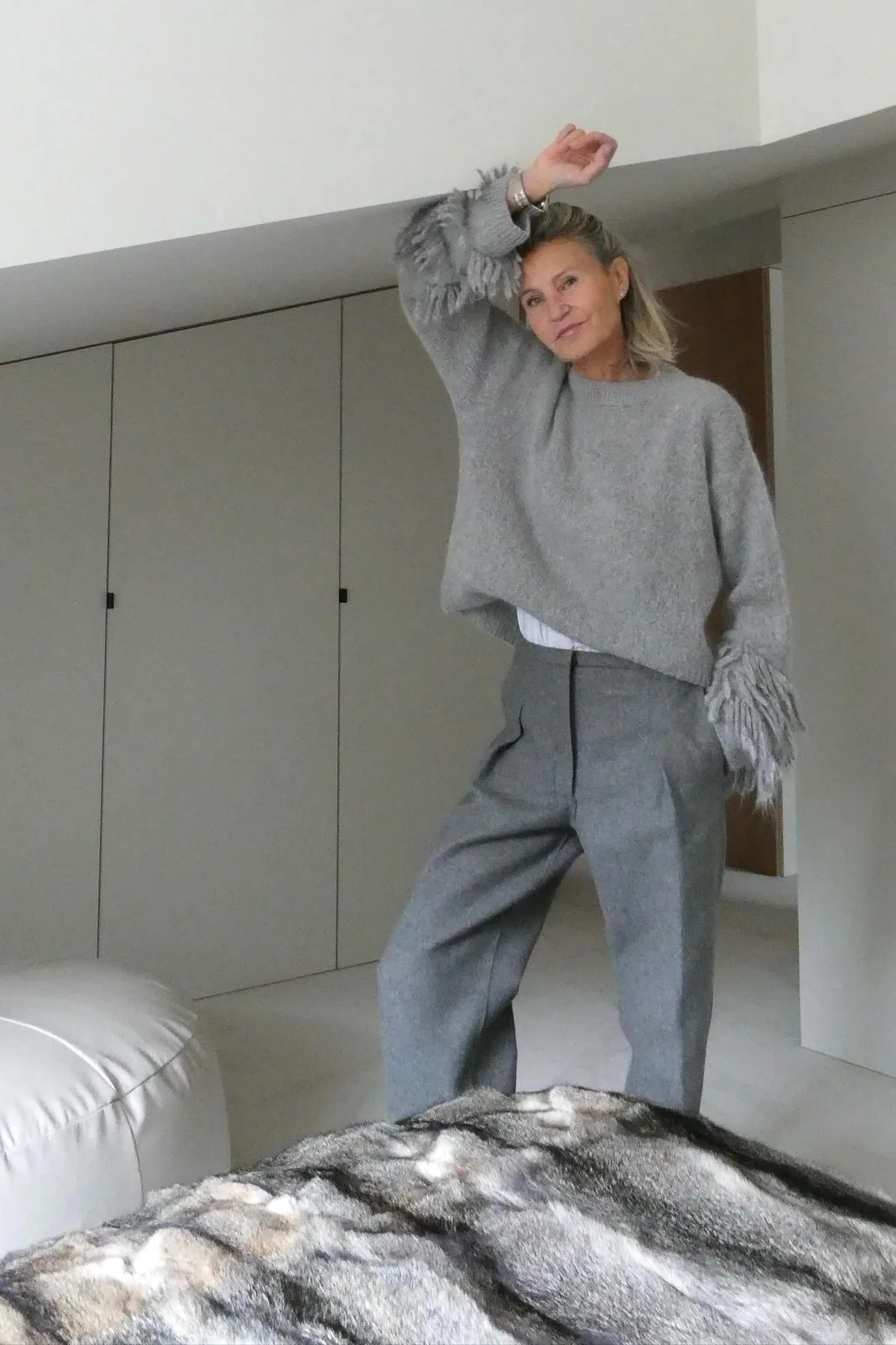 Woman over 50 in a silver-gray knit and black trousers with a moon pendant, a lunar priestess gothic Halloween costume.