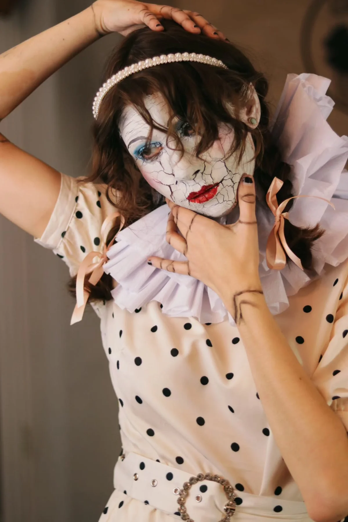 Woman in her 50s in an ivory lace dress with porcelain doll makeup and a painted face crack, a creepy porcelain doll solo horror Halloween costume