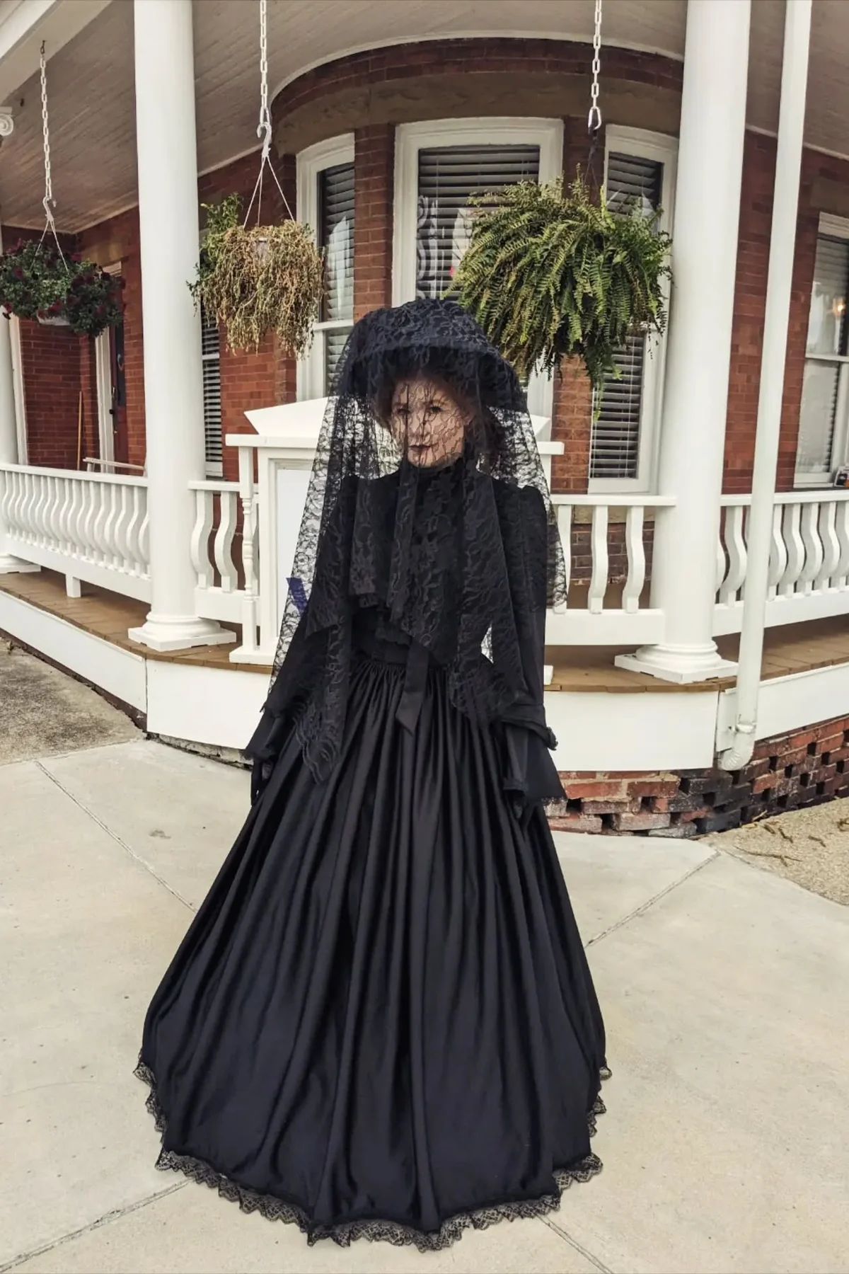 Woman in her 50s in a black velvet gown with a long mourning veil holding a dead lily, a haunted widow solo horror Halloween costume