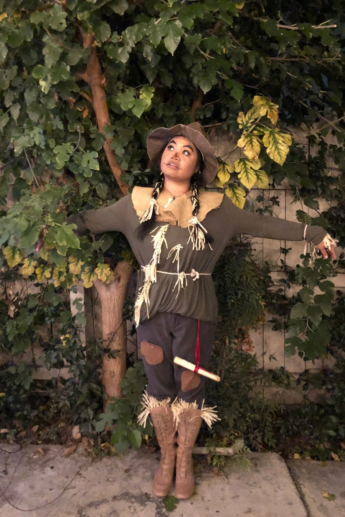 Woman in her 50s in patched flannel and overalls with stitched scarecrow face paint, a haunted scarecrow solo horror Halloween costume