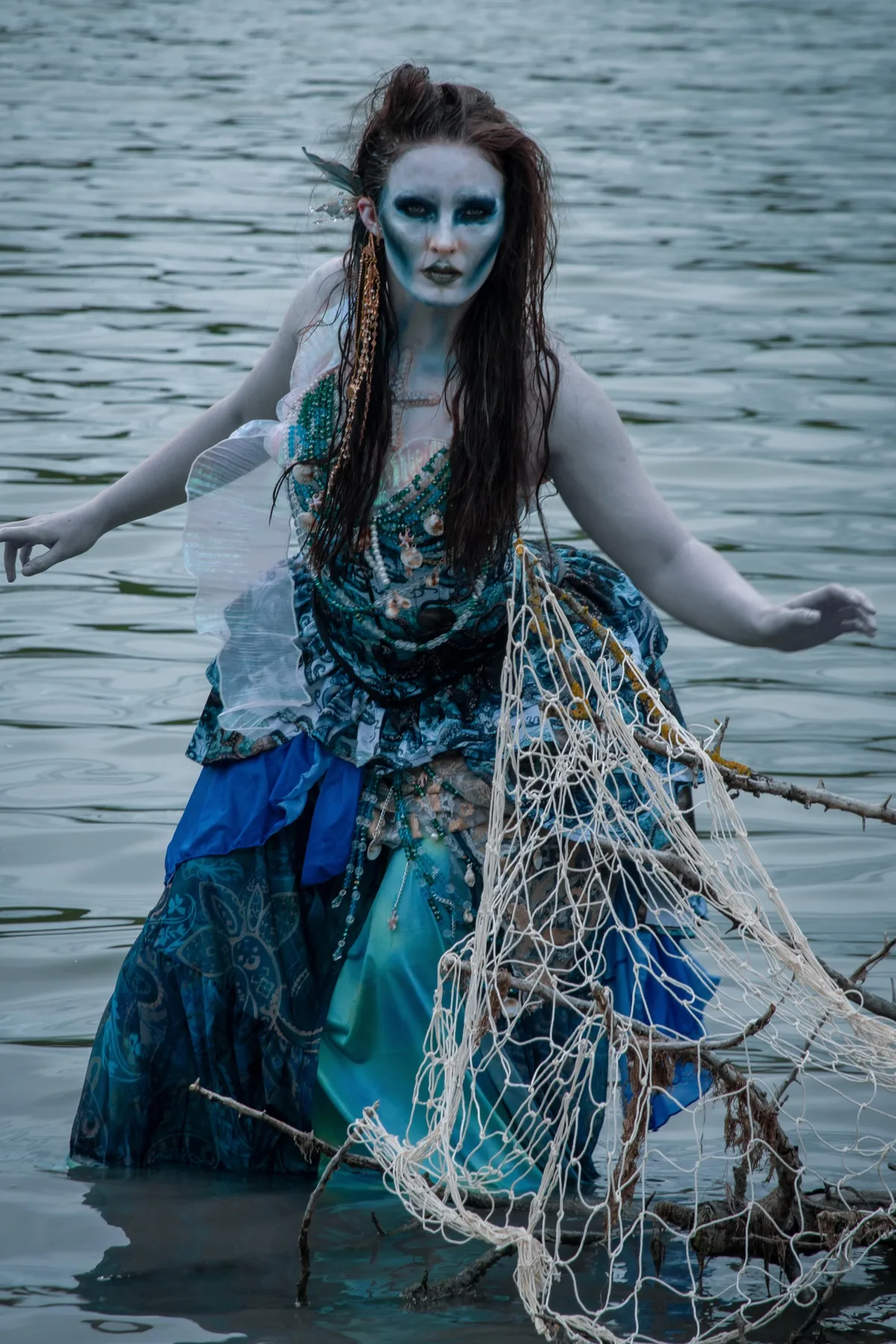Woman in her 50s in a tattered teal gown with seaweed and wet-look hair, a drowned siren solo horror Halloween costume