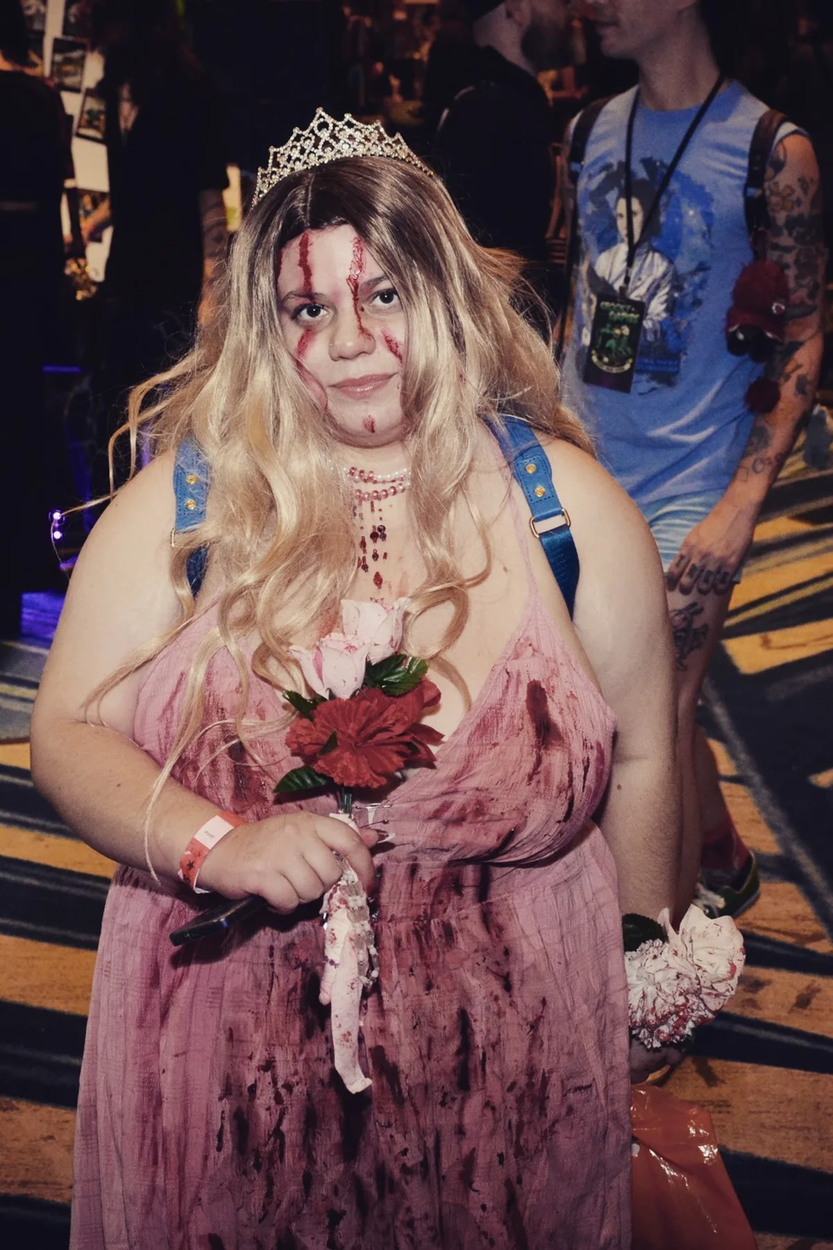 Woman in her 50s in a torn pink tulle prom dress with a crooked tiara and sash, a living dead prom queen solo horror Halloween costume