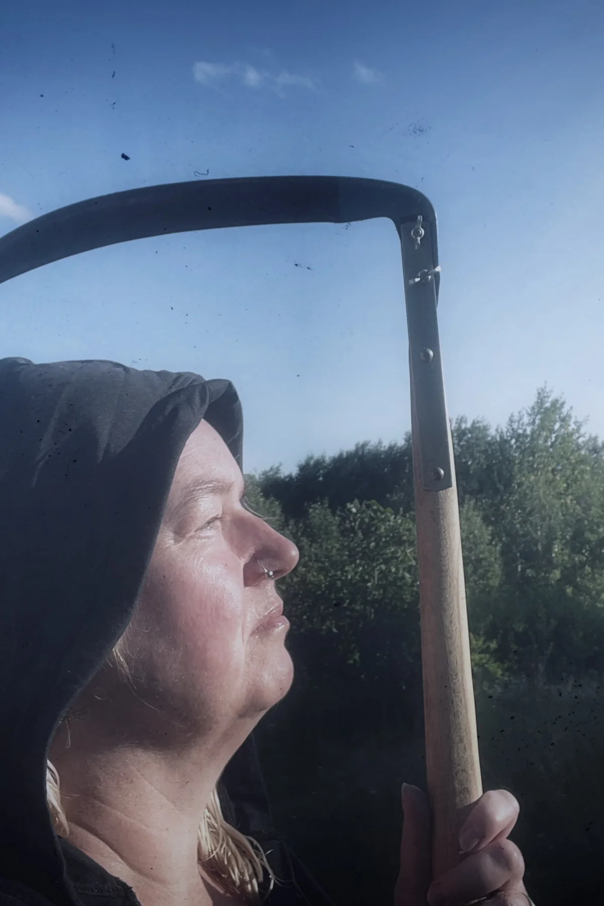 Woman in her 50s in a black hooded cloak holding a scythe in a foggy graveyard, a dark reaper solo horror Halloween costume