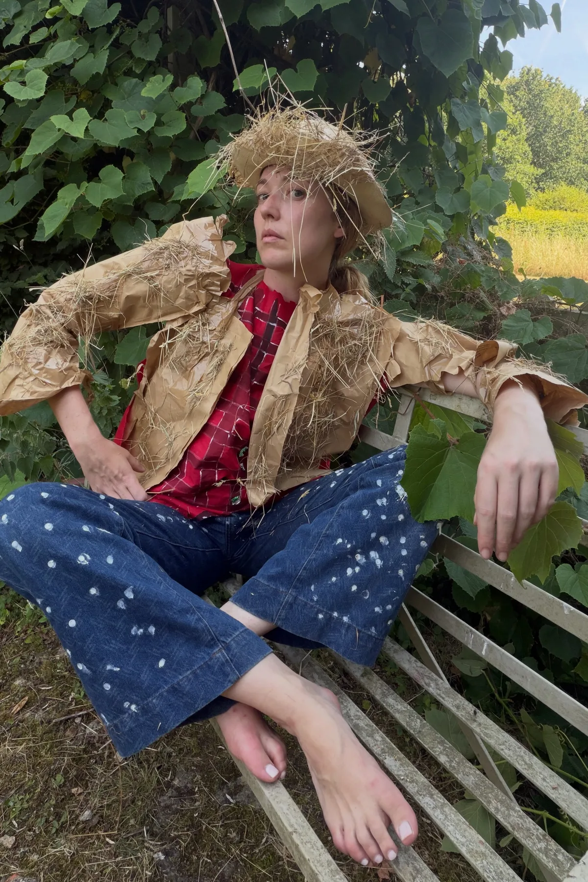 Woman in her 50s in overalls and a straw hat holding dead black flowers, a haunted gardener solo horror Halloween costume
