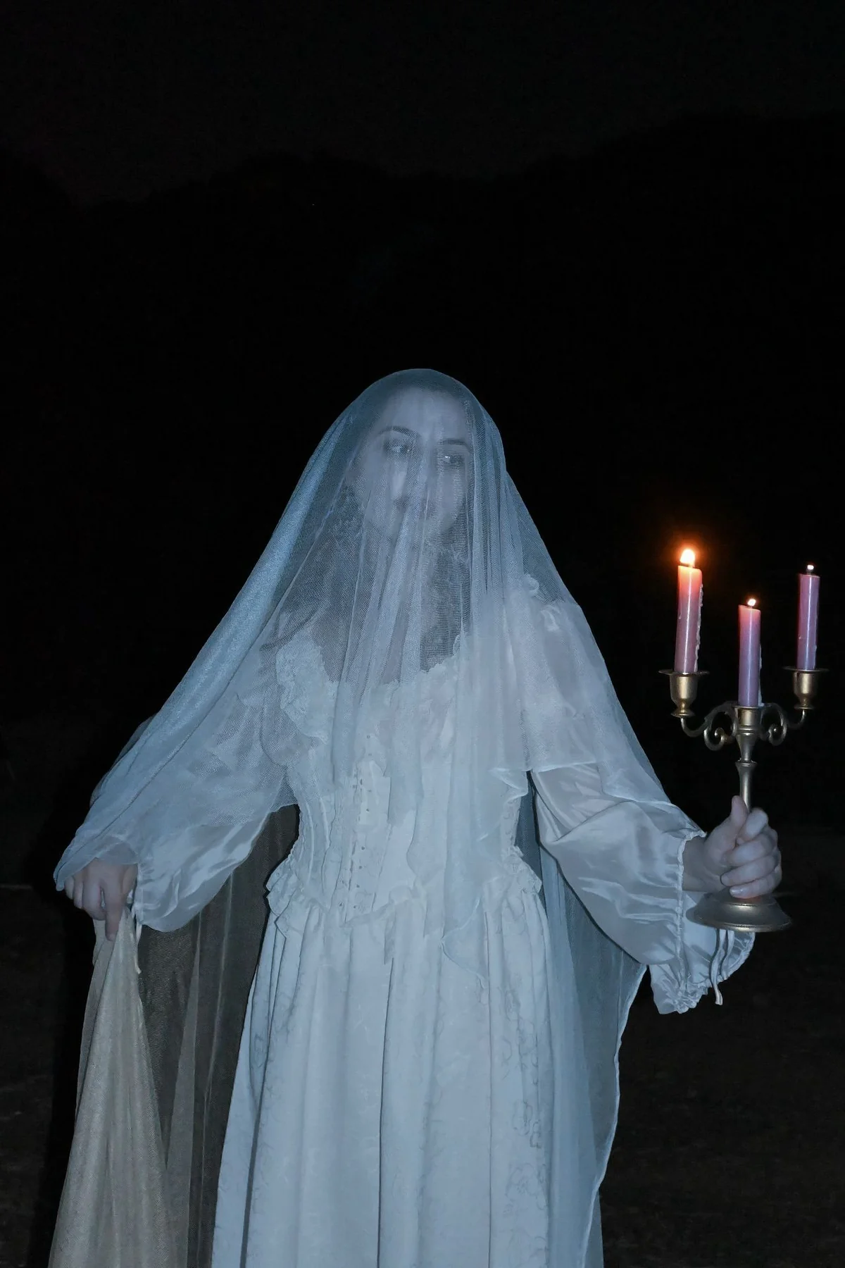Woman in her 50s in a white lace Victorian gown with a parasol on a dark staircase, a ghostly Victorian lady solo horror Halloween costume