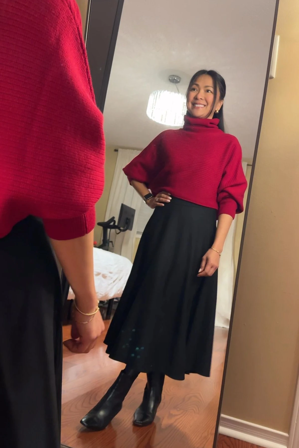 Woman in red turtleneck and black A-line midi skirt taking a mirror selfie at Christmas