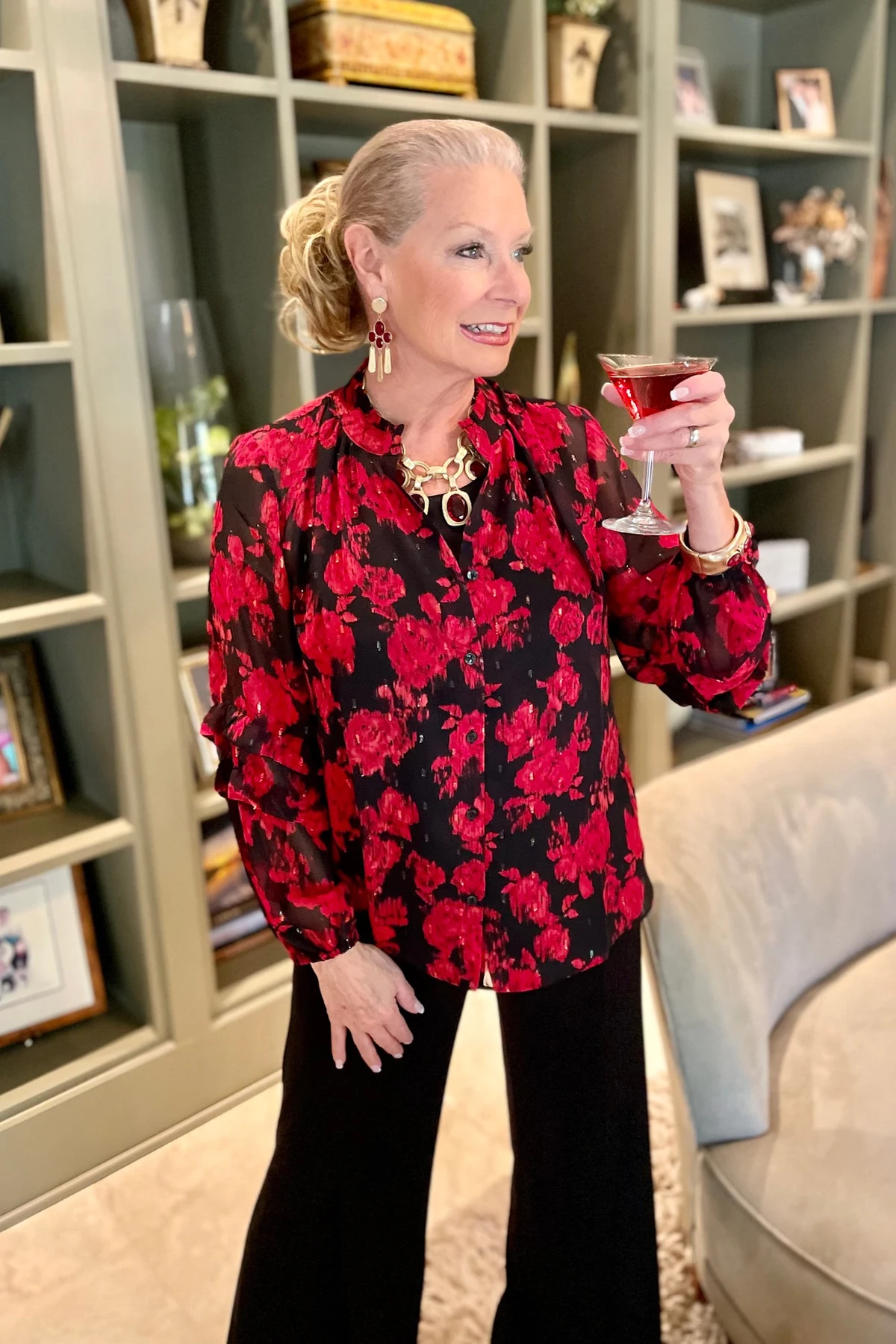 Woman in red floral blouse and black wide-leg trousers holding a cocktail at Christmas