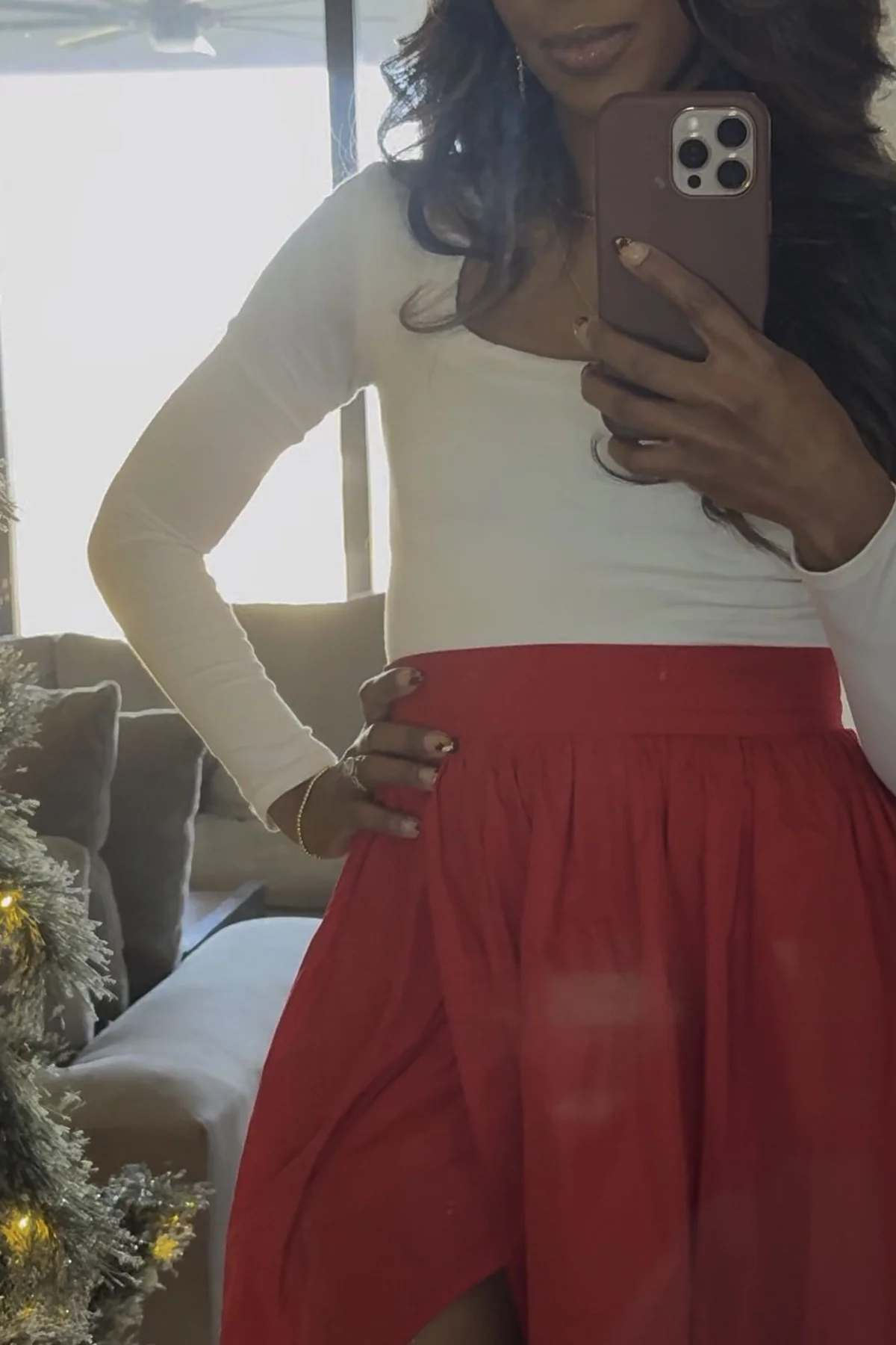 Woman in white top and red satin maxi skirt with thigh slit beside a Christmas tree