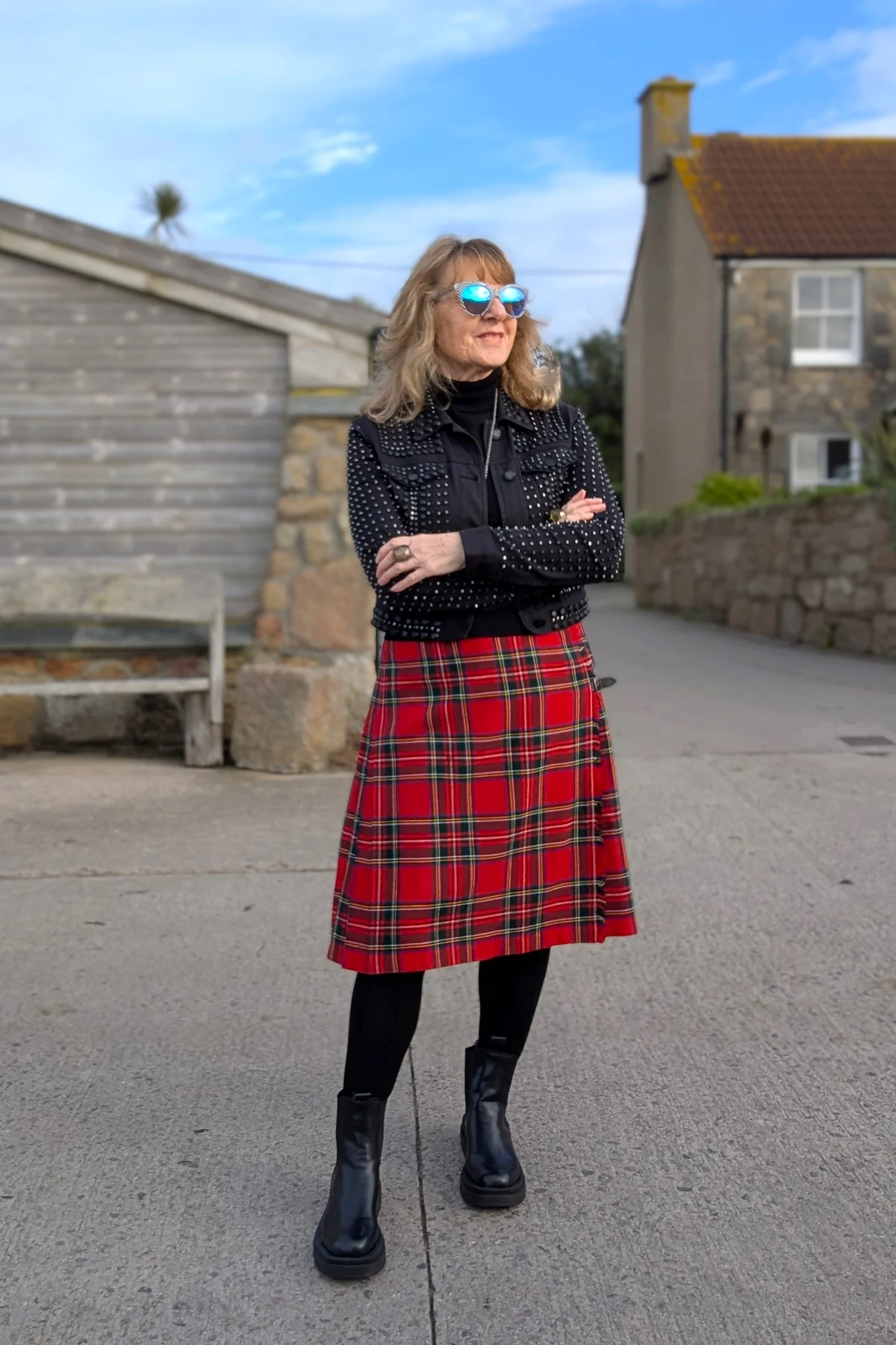 Woman in red tartan midi skirt, black turtleneck and studded jacket outdoors