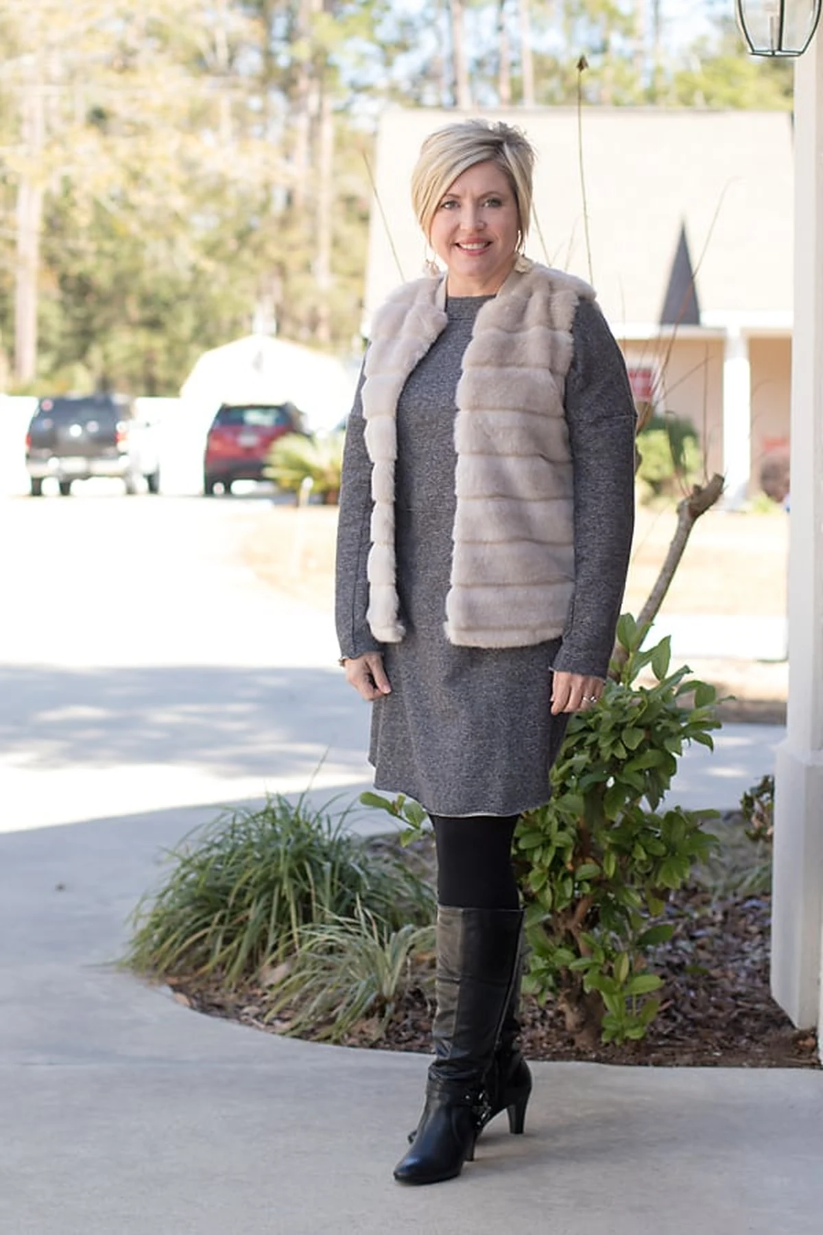 Woman in cream faux-fur vest over gray sweater dress at Christmas