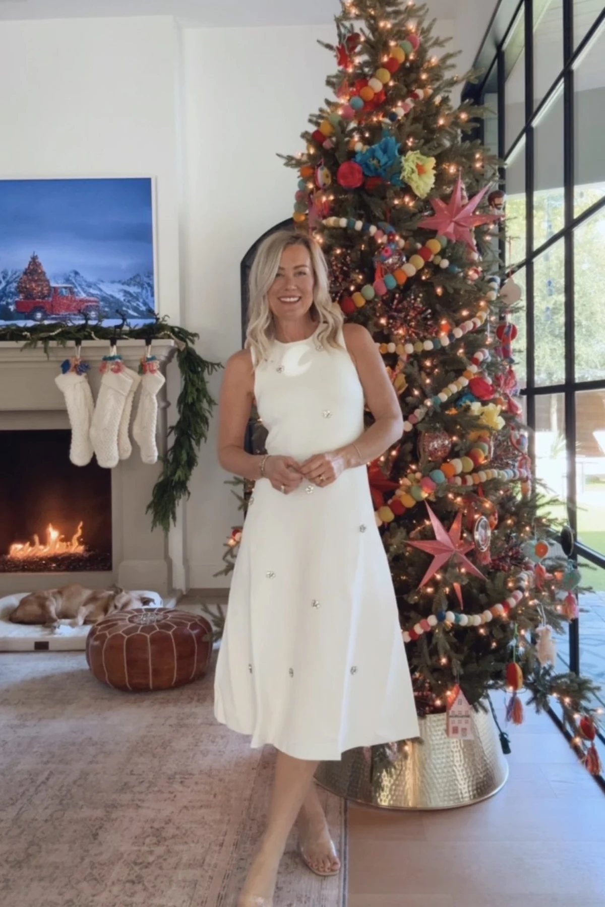 Woman in ivory embellished fit-and-flare dress by a Christmas tree and fireplace