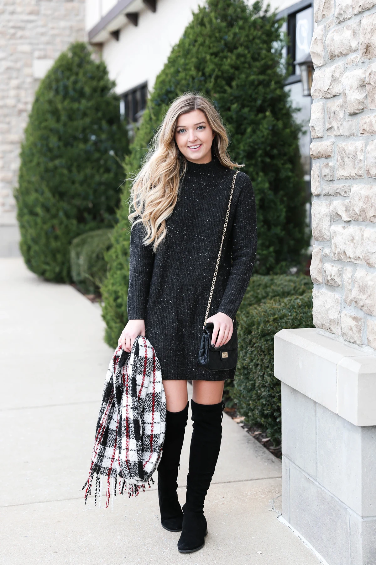 Woman in black sweater dress and plaid blanket scarf at Christmas