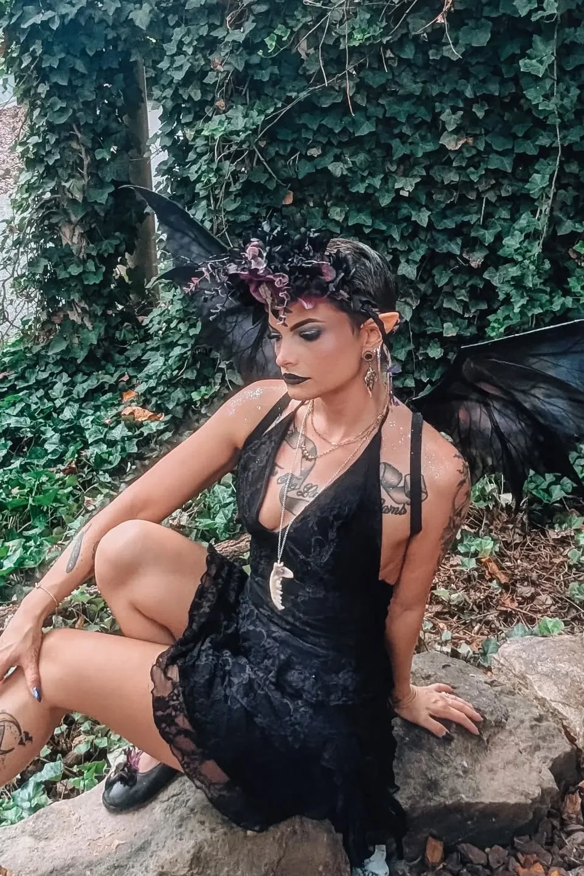 Woman in a black lace dress with large dark fairy wings and floral headpiece, a raven feather dark fairy gothic Halloween costume