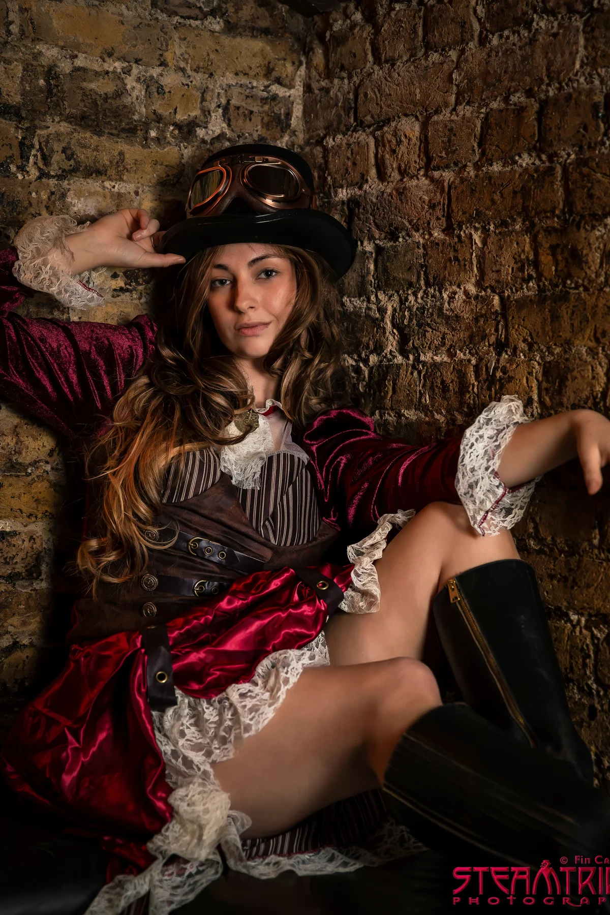 Woman in a burgundy velvet blouse, brown corset and top hat with goggles, a gothic steampunk lady Halloween costume